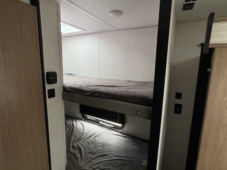 Inside an rv rental, showing a bunk bed sleeping area with two stacked beds, bedding, a window, and wall controls.. Forest River Primetime Avenger LT 2022