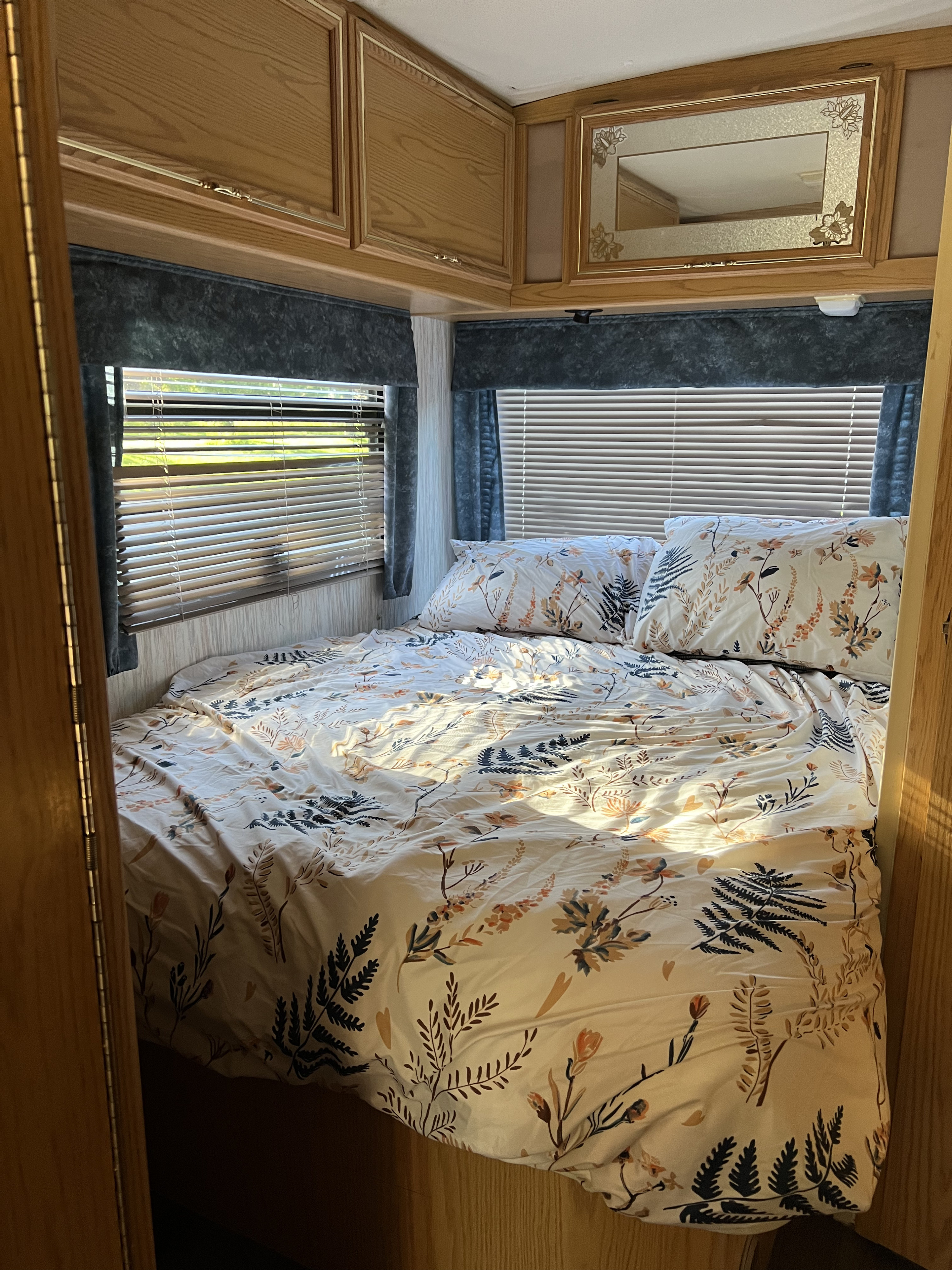 Inviting RV rental bedroom with botanical duvet, oak cabinets, and sunlit windows. Perfect for your next adventure!. Winnebago Brave 1995