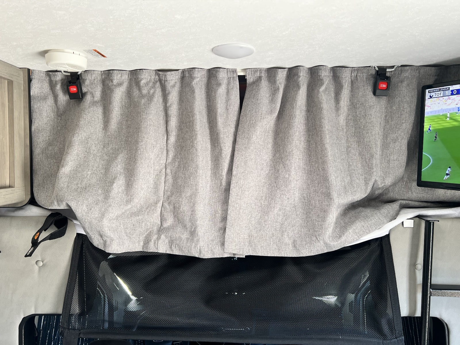 RV rental interior features: gray privacy curtains, TV (soccer game), smoke detector, ceiling light, and mesh storage below.. Forest River Coachmen Cross Trail XL 2022