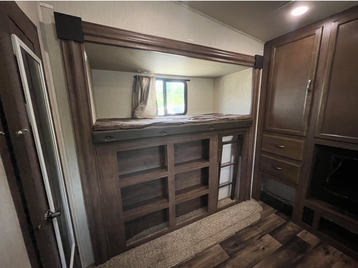 Cozy rv rental interior: dark wood bunk beds with window, ladder, and integrated shelving provide a compact sleeping and storage area.. Forest River Sandpiper 2020