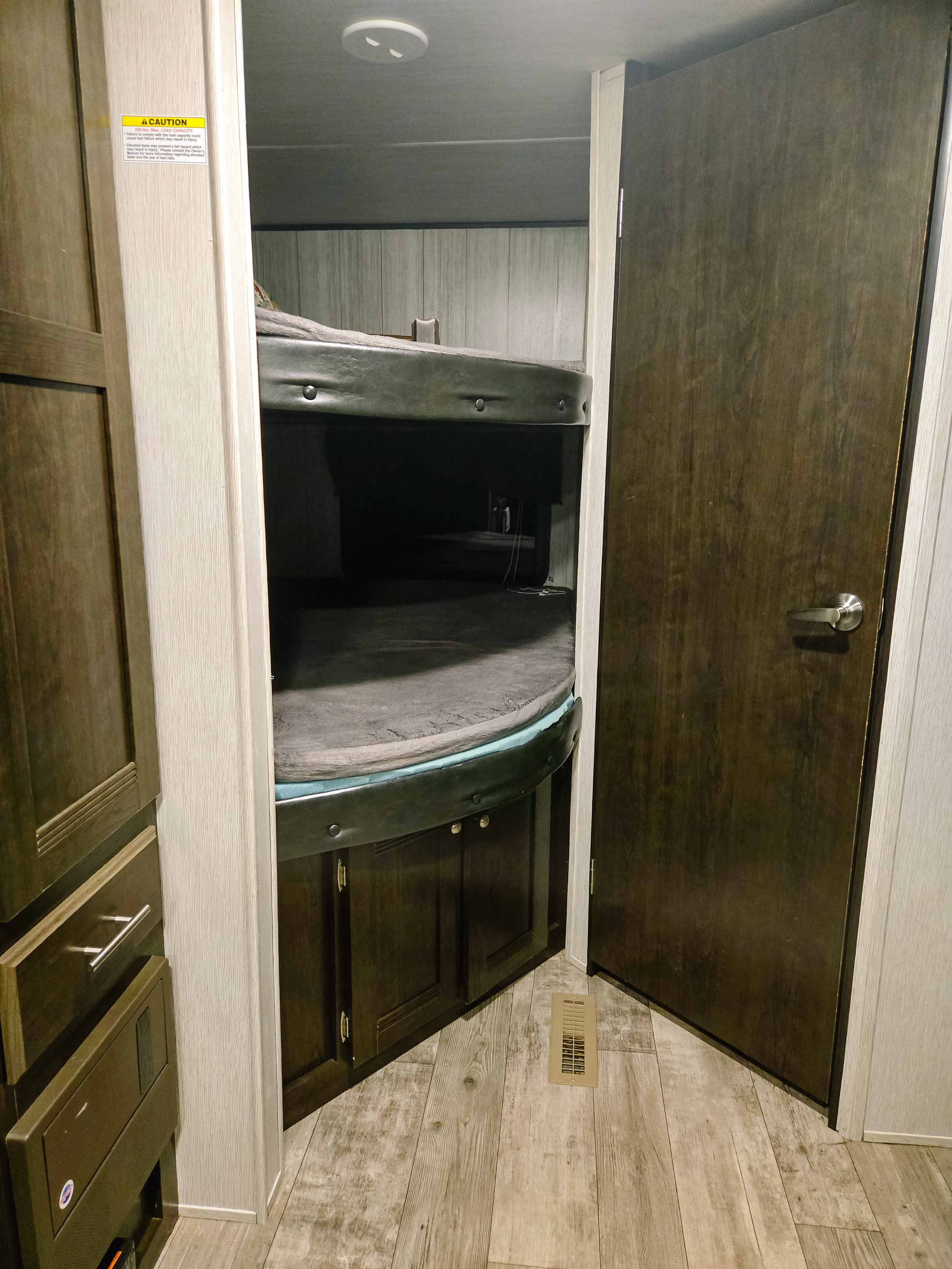 RV rental interior with dark wood bunk beds, cabinetry, and a door. A caution sticker is visible near the bunks.. Heartland RVs Pioneer 2019