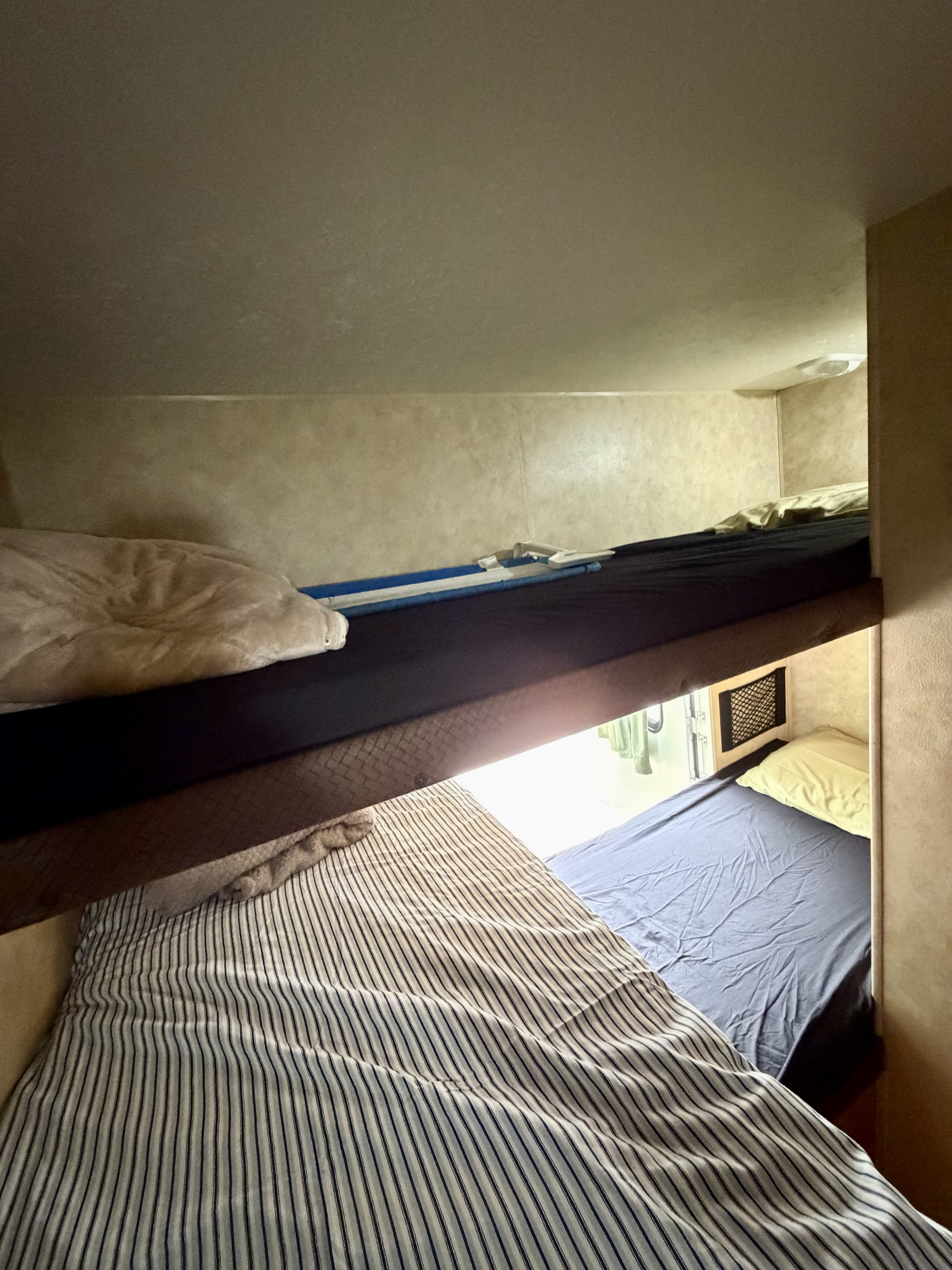 Inside an RV rental, compact bunk beds with a safety rail and varied bedding offer a practical sleeping space.. Sportsmen Sportsmen Trailer 2008