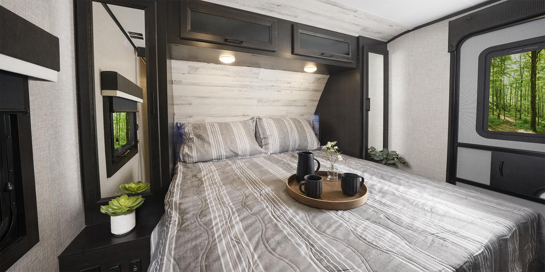 Cozy RV rental bedroom with striped bedding, nature views, and overhead storage. Perfect for a travel adventure.. Jayco Jay Feather 2023
