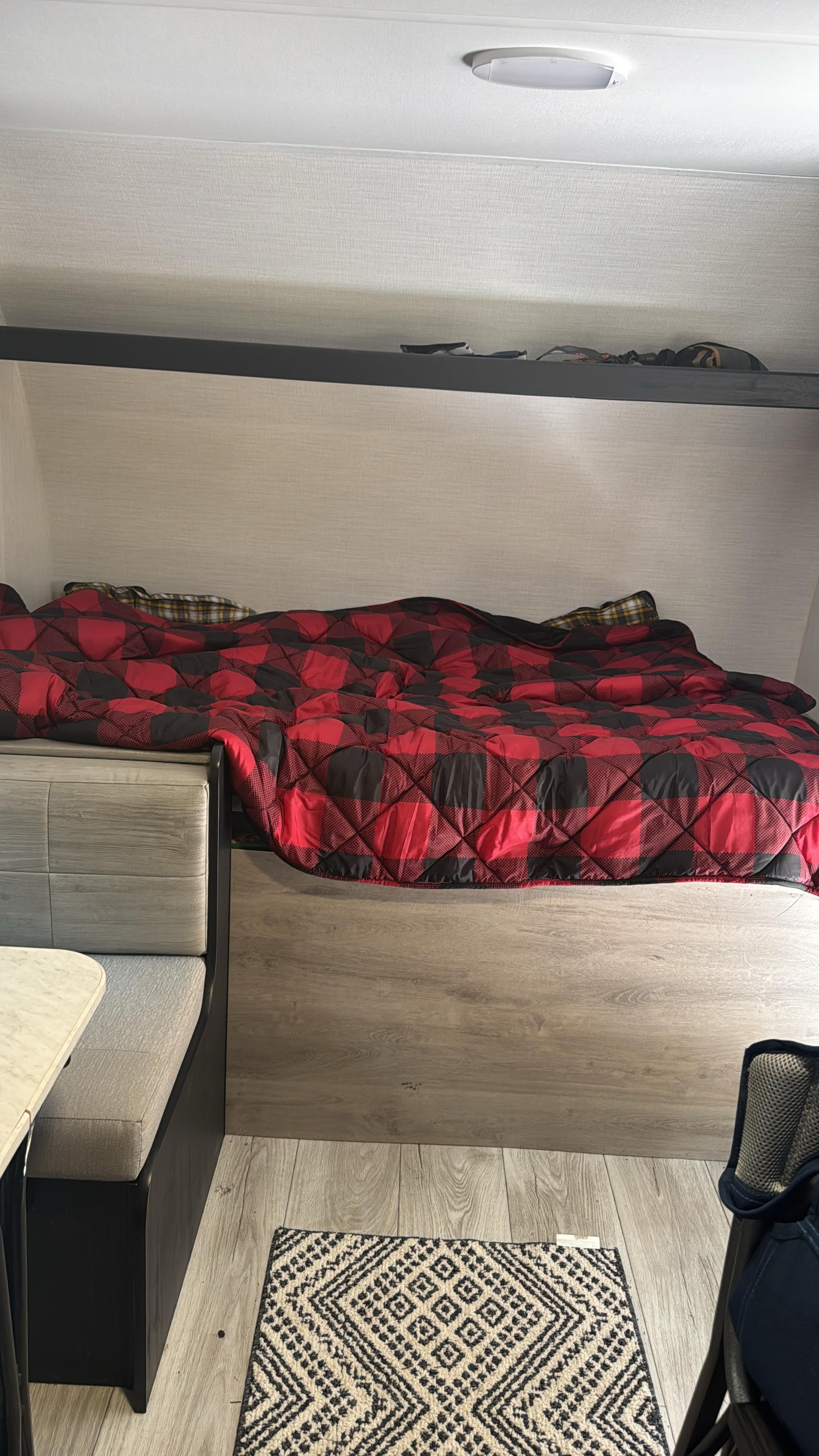 Cozy RV rental interior featuring a bunk bed with red plaid comforter, dinette, and patterned rug on wood-look floor.. Heartland RVs Prowler Lynx 2024
