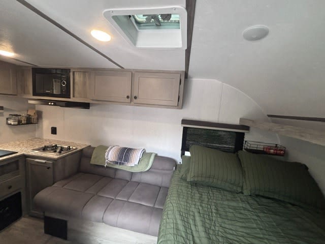 Cozy RV rental interior featuring a compact kitchen, L-shaped seating area, and a bed with green bedding.. Sunset Park RV Sun Lite LTD 13MJ 2025