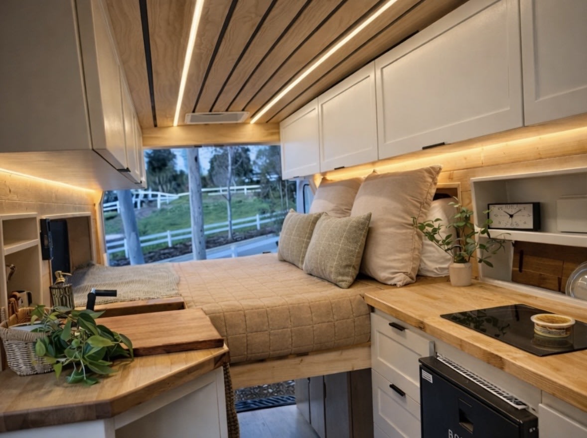 Cozy RV rental interior with a comfy bed, wood-paneled ceiling, and modern kitchen. Perfect for van life adventures!. Ford Transit 2023