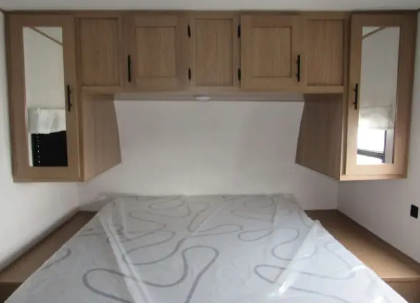 Clean RV rental bedroom featuring a bed with a fresh mattress, light wood overhead cabinets, and mirrored doors for storage.. Avenger Avenger Trailer 2022