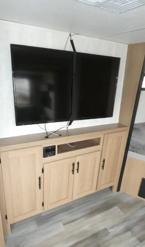 RV rental interior: Wall-mounted TV with security strap over light wood entertainment center and storage cabinetry.. Avenger Avenger Trailer 2022