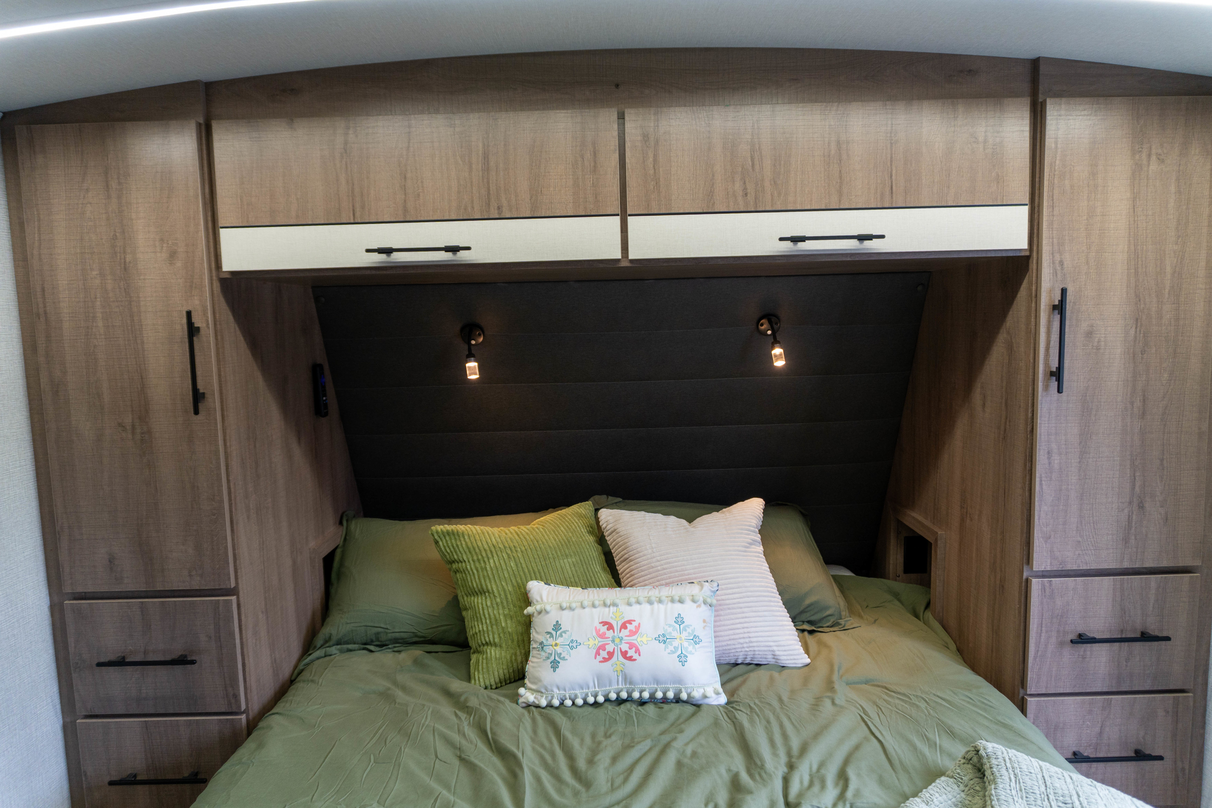 RV rental interior: A compact bedroom with a bed, green bedding, soft pillows, wooden storage cabinets, and warm reading lights.. Grand Design Imagine 2024