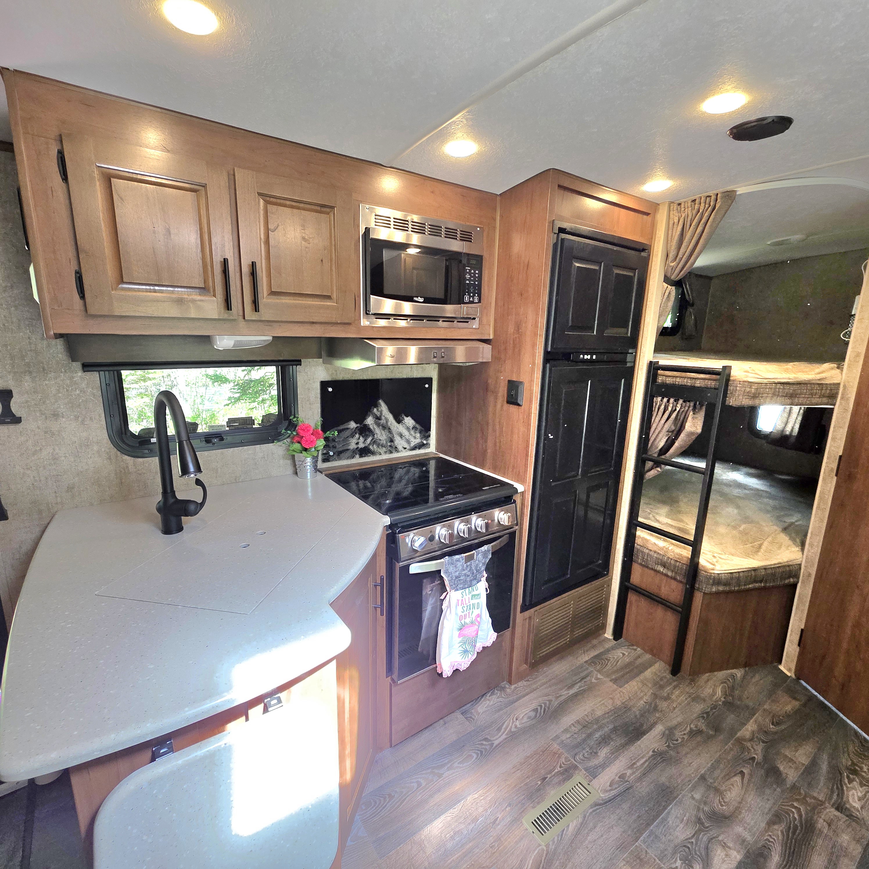 This rv rental offers a well-equipped kitchen with sink, microwave, stove/oven, fridge, and warm wood cabinets, plus bunk beds.. Outdoors RV 23DBS 2023