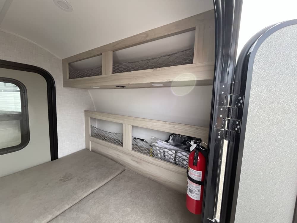 RV rental interior featuring a compact sleeping area with cushions, overhead storage, and a fire extinguisher for safety.. Bontrager Outdoors Bontrager Outdoors Trailer 2026