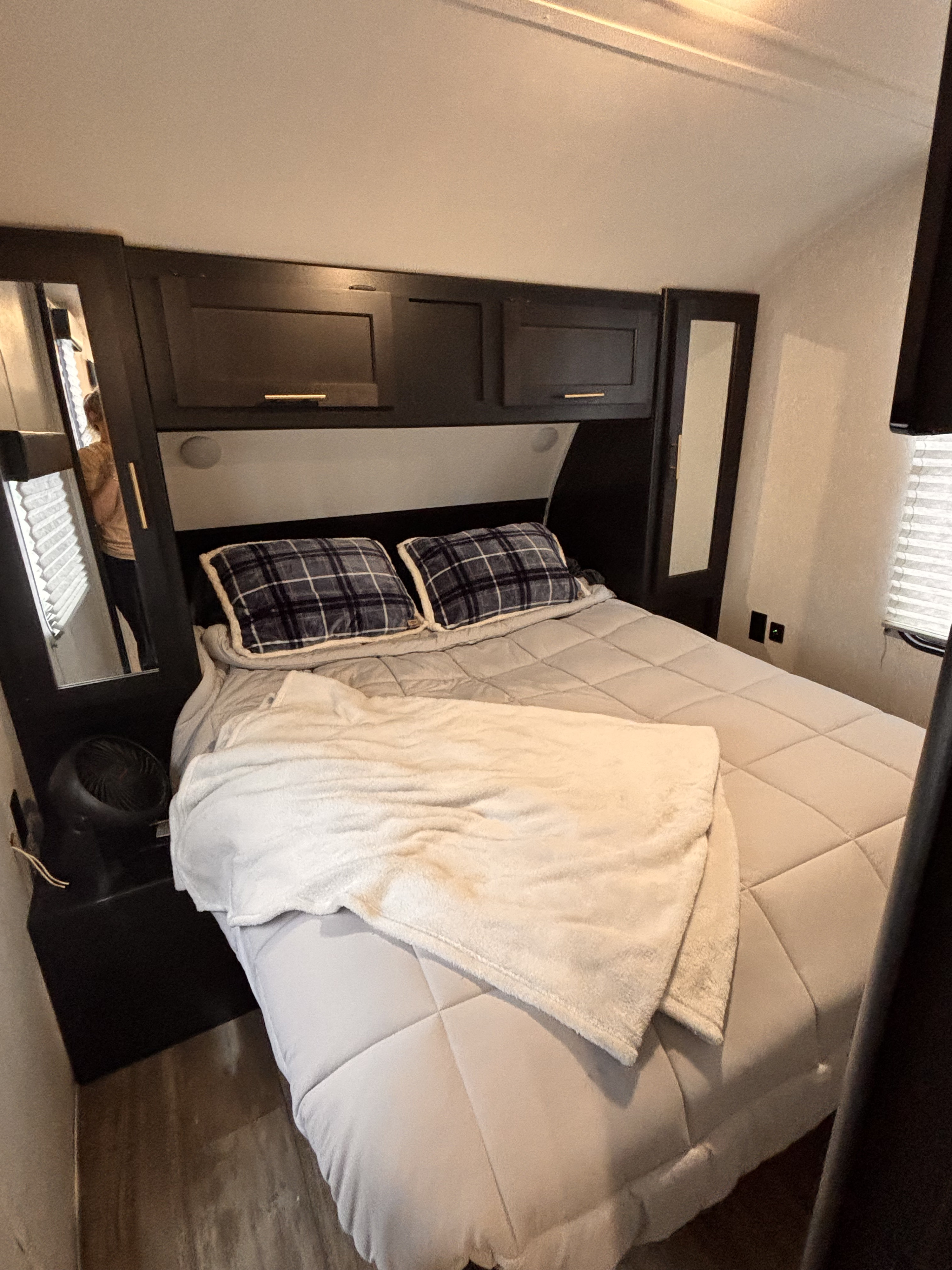 Cozy RV rental bedroom featuring a full bed with plaid pillows, overhead cabinets, and side mirrors, perfect for travel.. Forest River Cherokee Grey Wolf 2021
