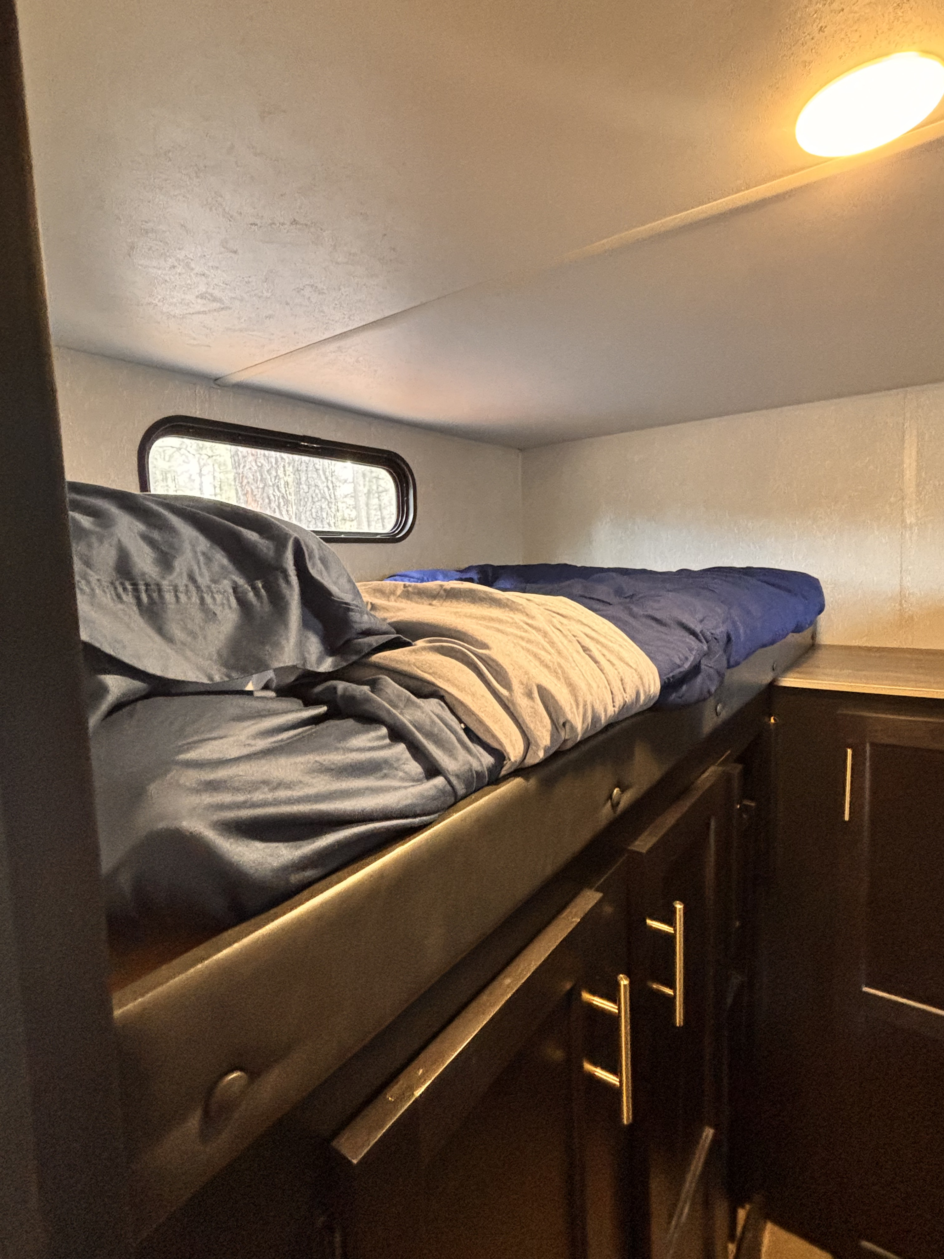 This RV rental features a cozy bunk bed with blue bedding, a window view, and dark storage cabinets below for camping.. Forest River Cherokee Grey Wolf 2021