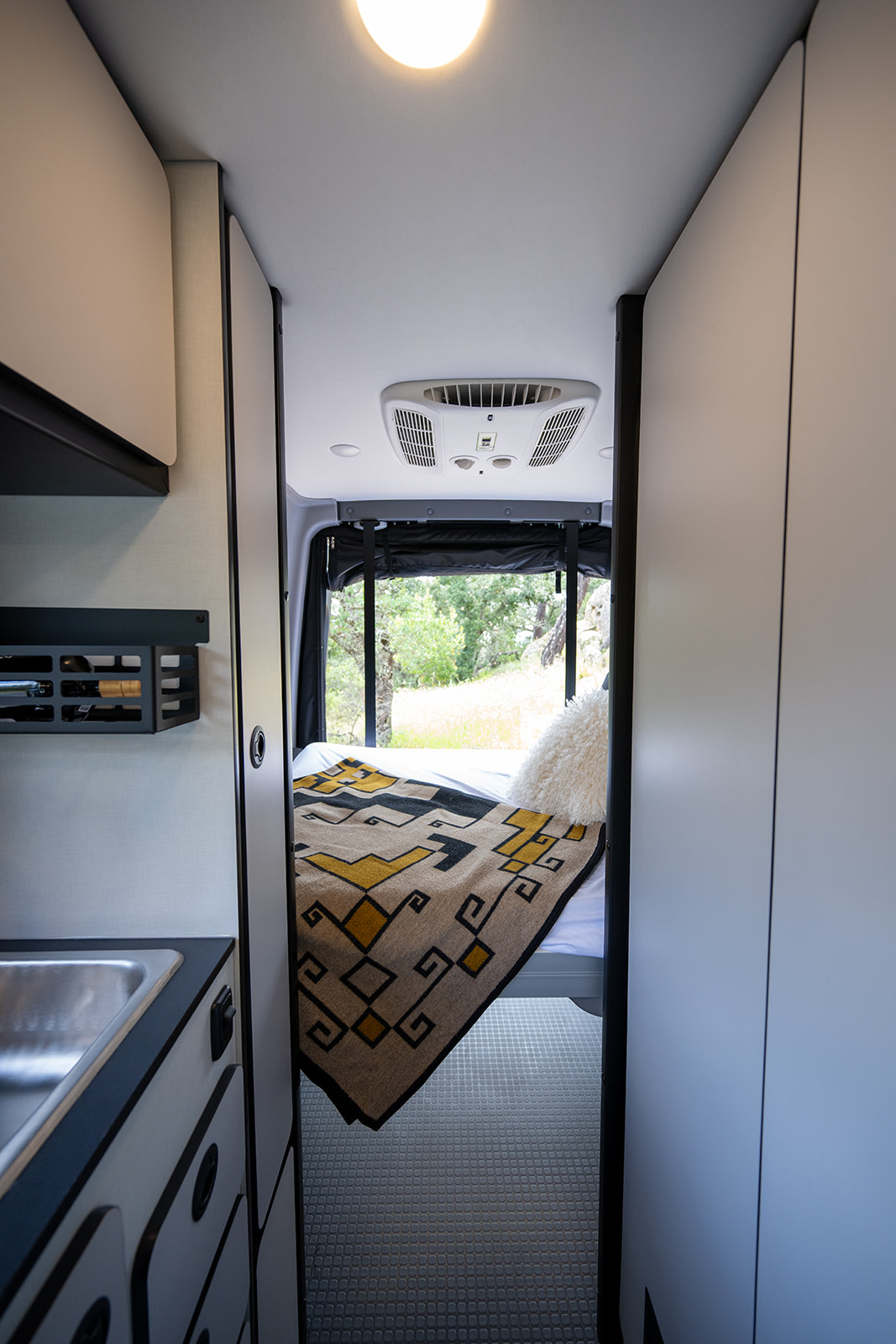 Explore this RV rental's modern interior: cozy bed, sink area, AC unit, and natural views outside. Ideal for adventures.. Winnebago Revel 2026
