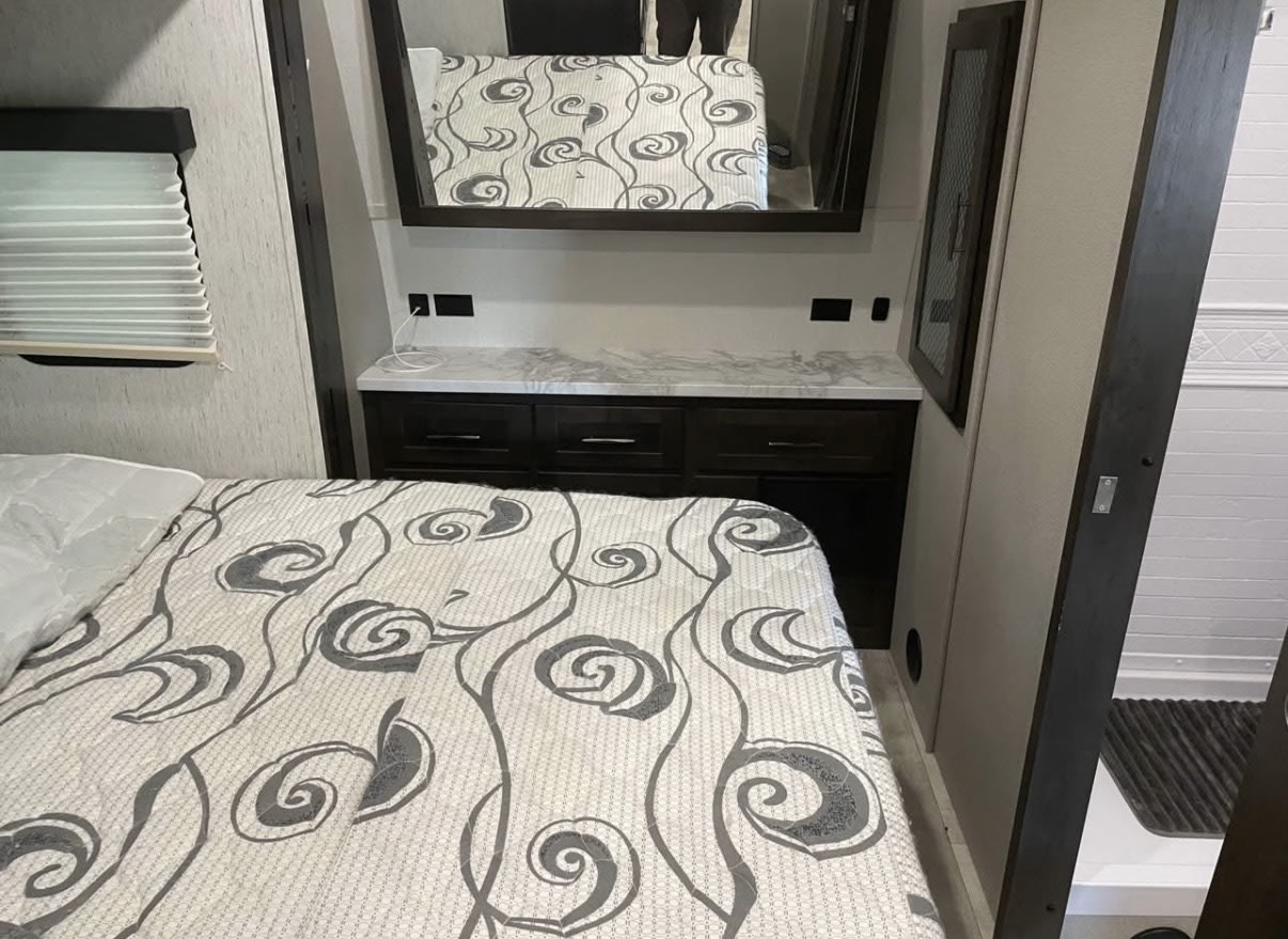 RV rental bedroom: comfortable bed, practical storage dresser with mirror, window blinds, and adjacent shower for travel convenience.. Grand Design Momentum 2021
