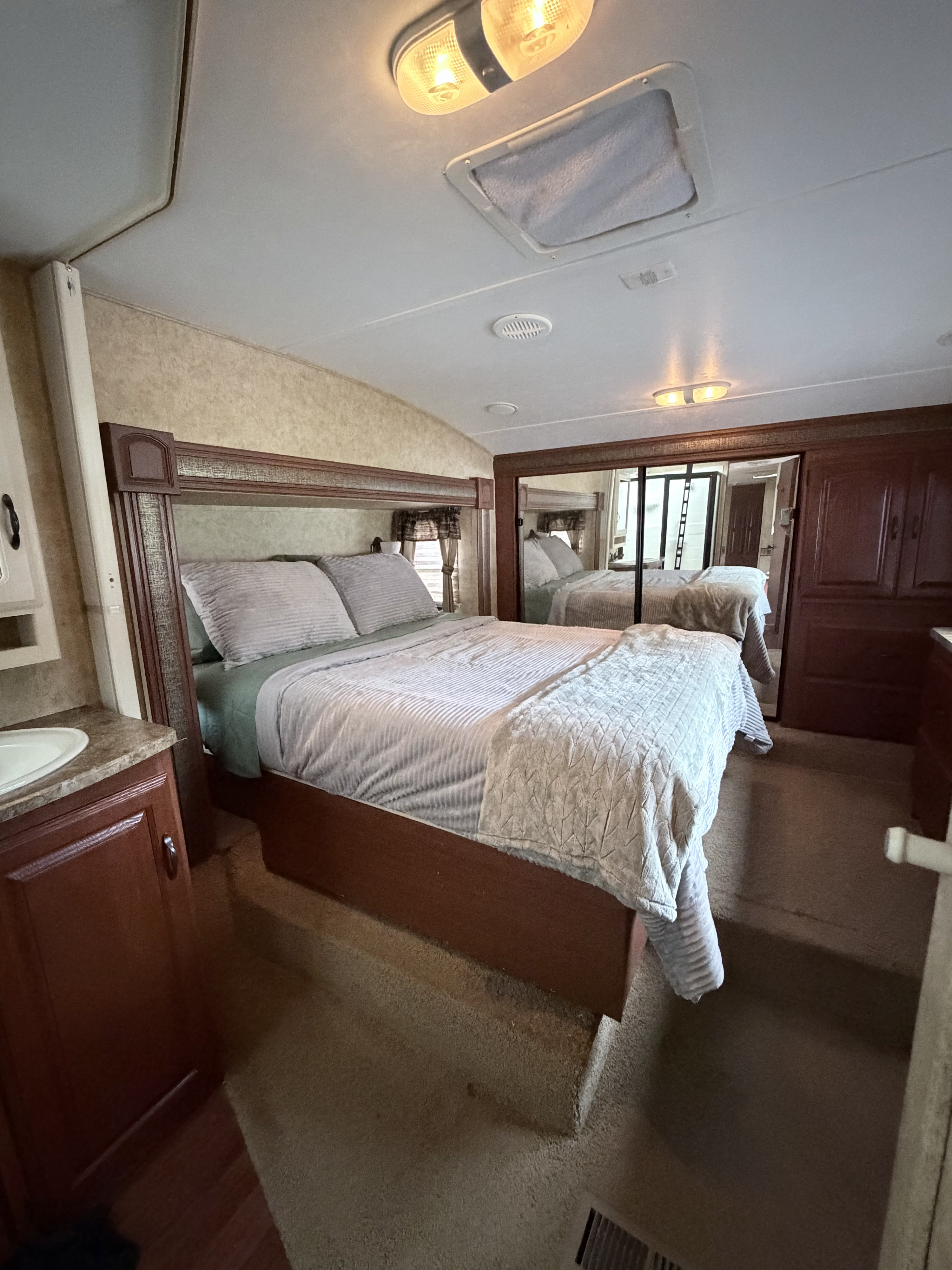 Cozy RV rental bedroom featuring a comfortable bed, mirrored wardrobe, vanity, and integrated lighting in this functional space.. Keystone RV Outback 2010