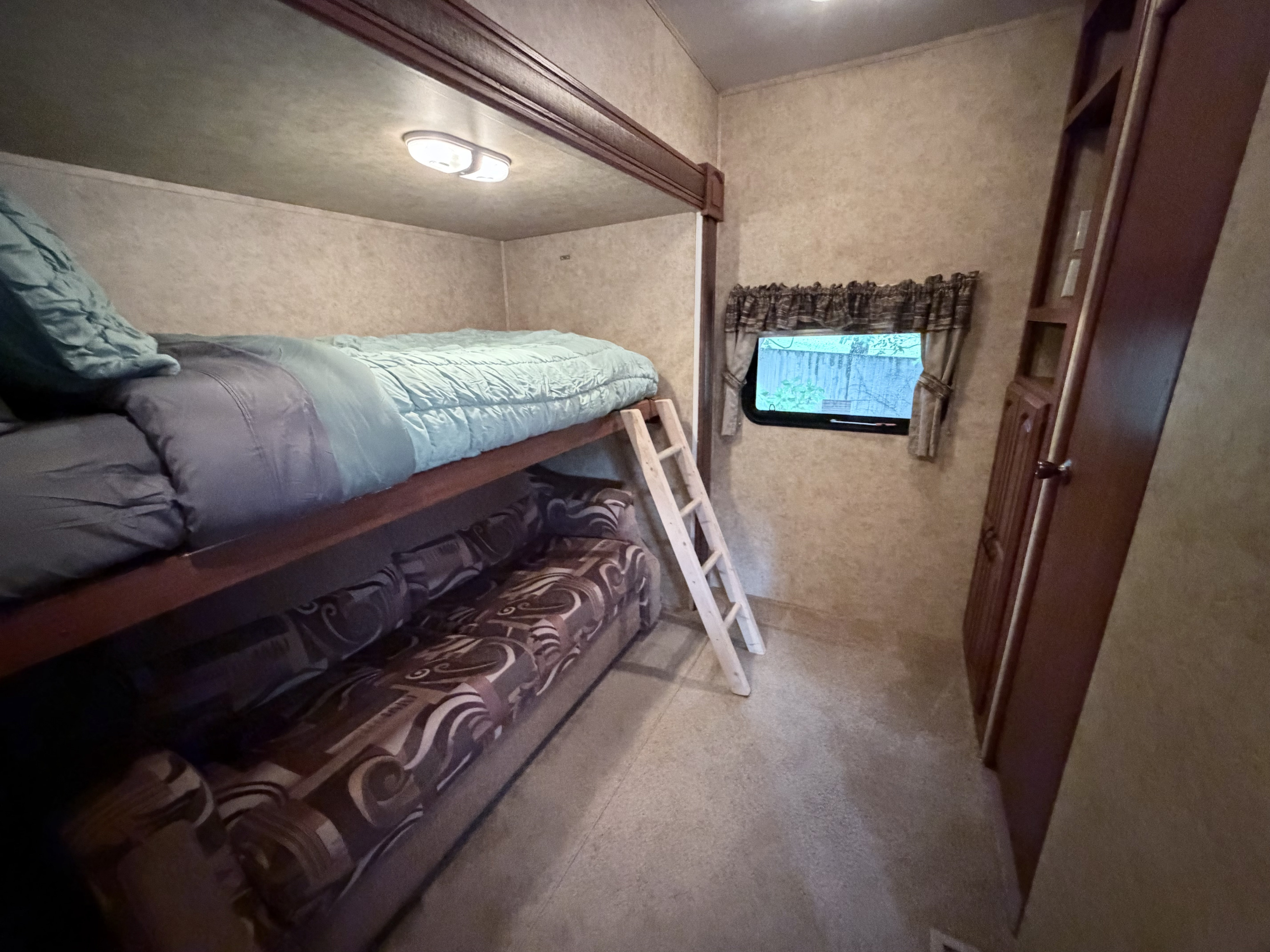 RV rental bunk beds: upper bed with blue bedding, lower convertible sofa, and ladder, plus window. Cozy sleeping space.. Keystone RV Outback 2010