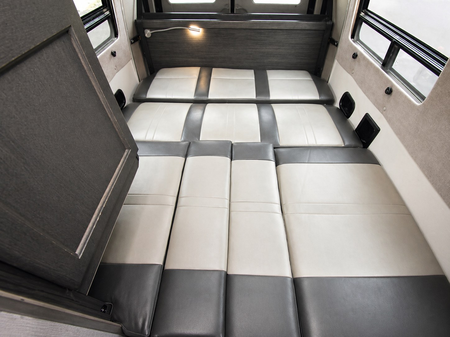 Spacious RV rental interior featuring a comfortable convertible bed with two-tone grey and off-white cushions, ideal for travel.. Roadtrek Roadtrek Class B 2015