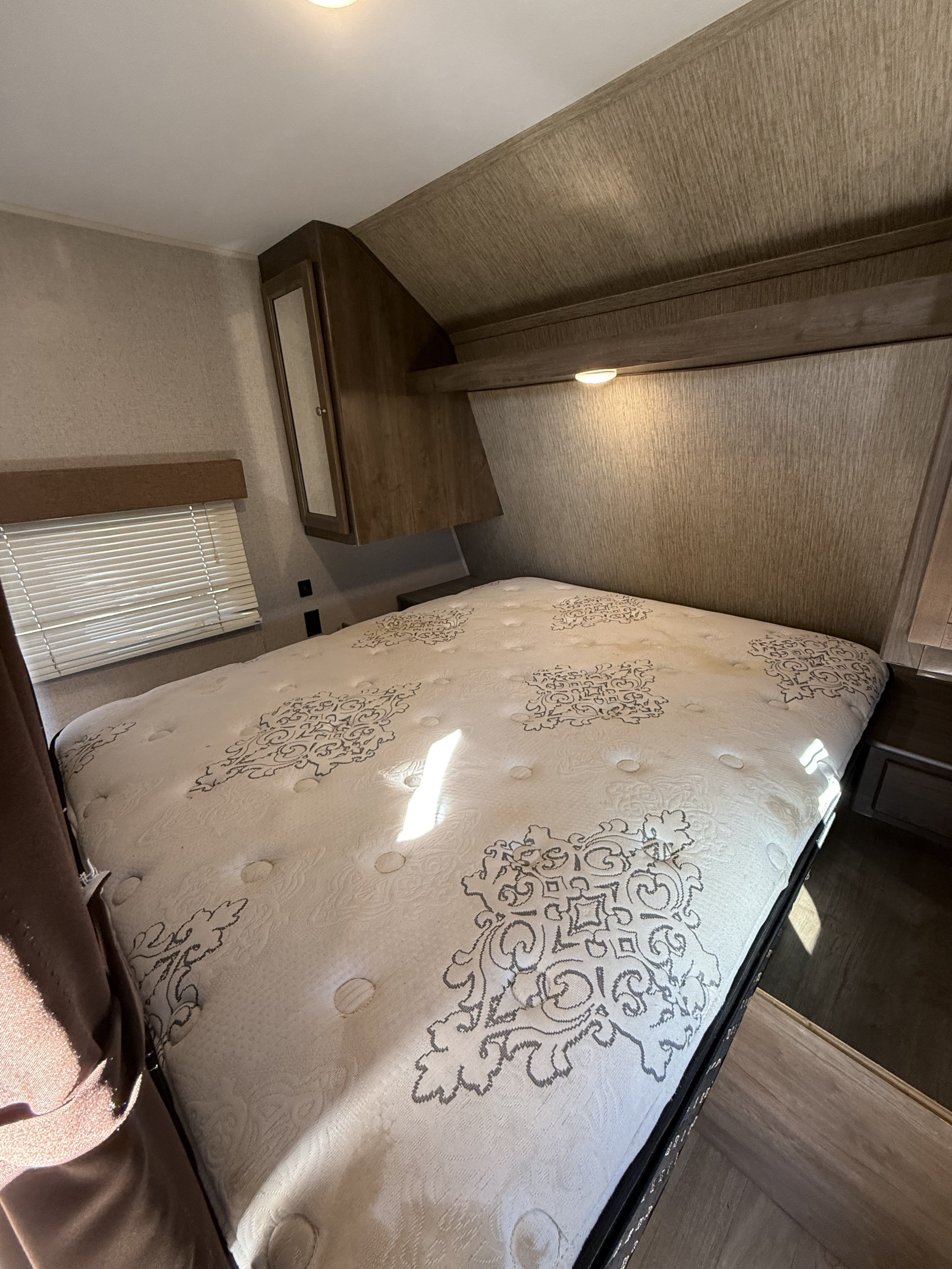 Comfortable RV rental bedroom featuring a mattress with ornate pattern, overhead storage, and window blinds for your journey.. Coleman 262BH 2019