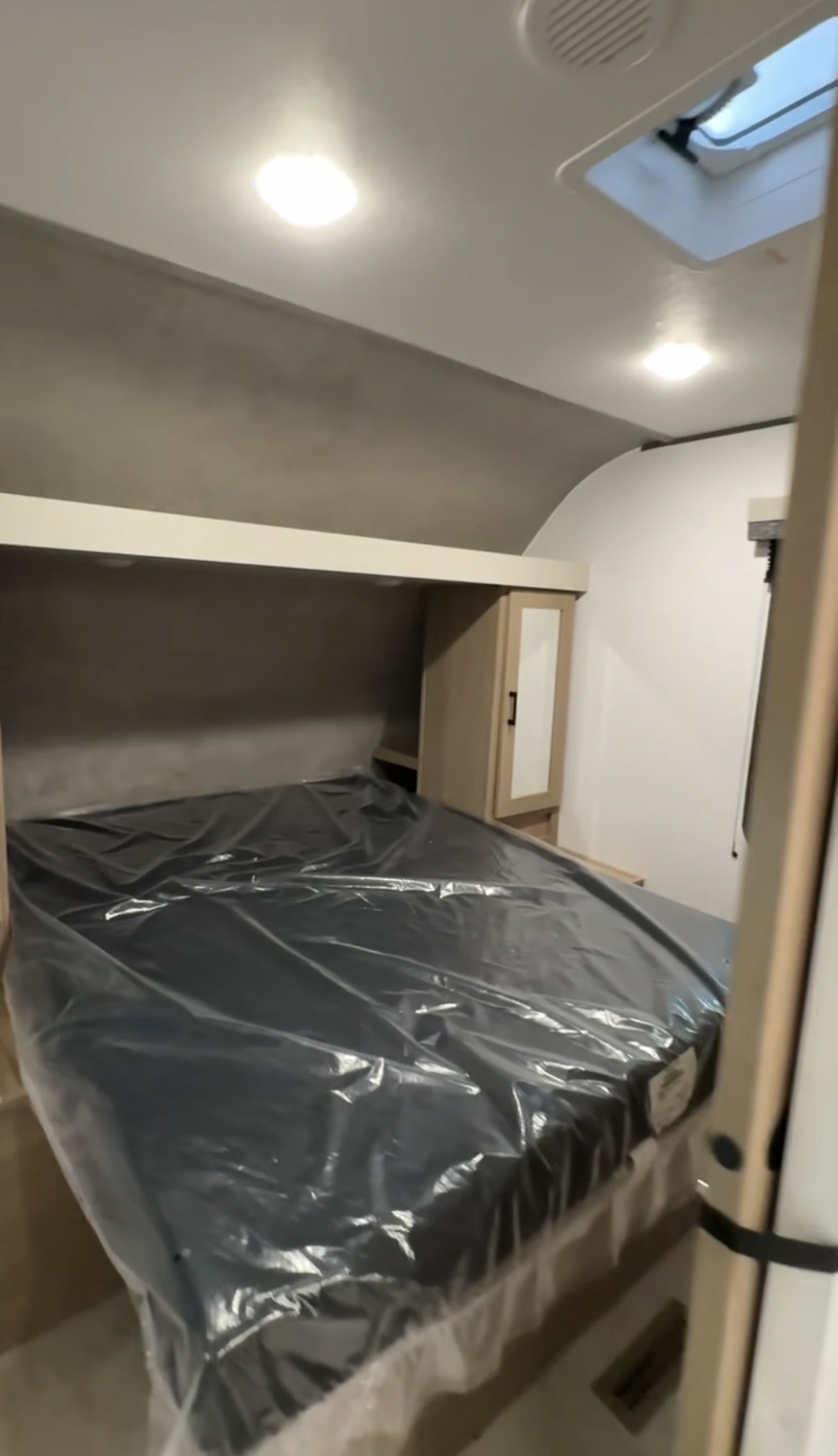 Compact rv rental bedroom featuring a new, plastic-covered bed, overhead storage, and a narrow wardrobe.. Aspen Trail 29tb 2026