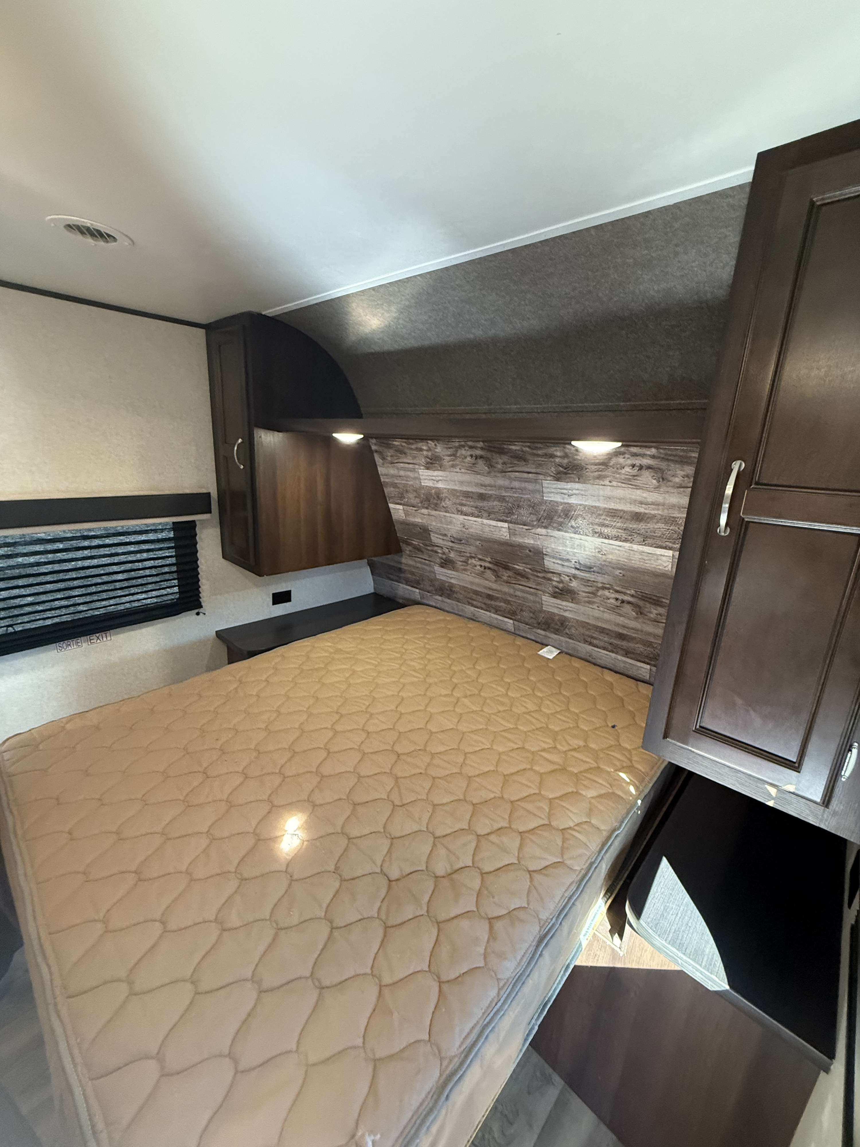RV rental sleeping area: features a bed, dark wood cabinets, window with blinds, and a wood-look headboard for a cozy interior.. Jayco Jay Flight SLX Baja Edition 2018