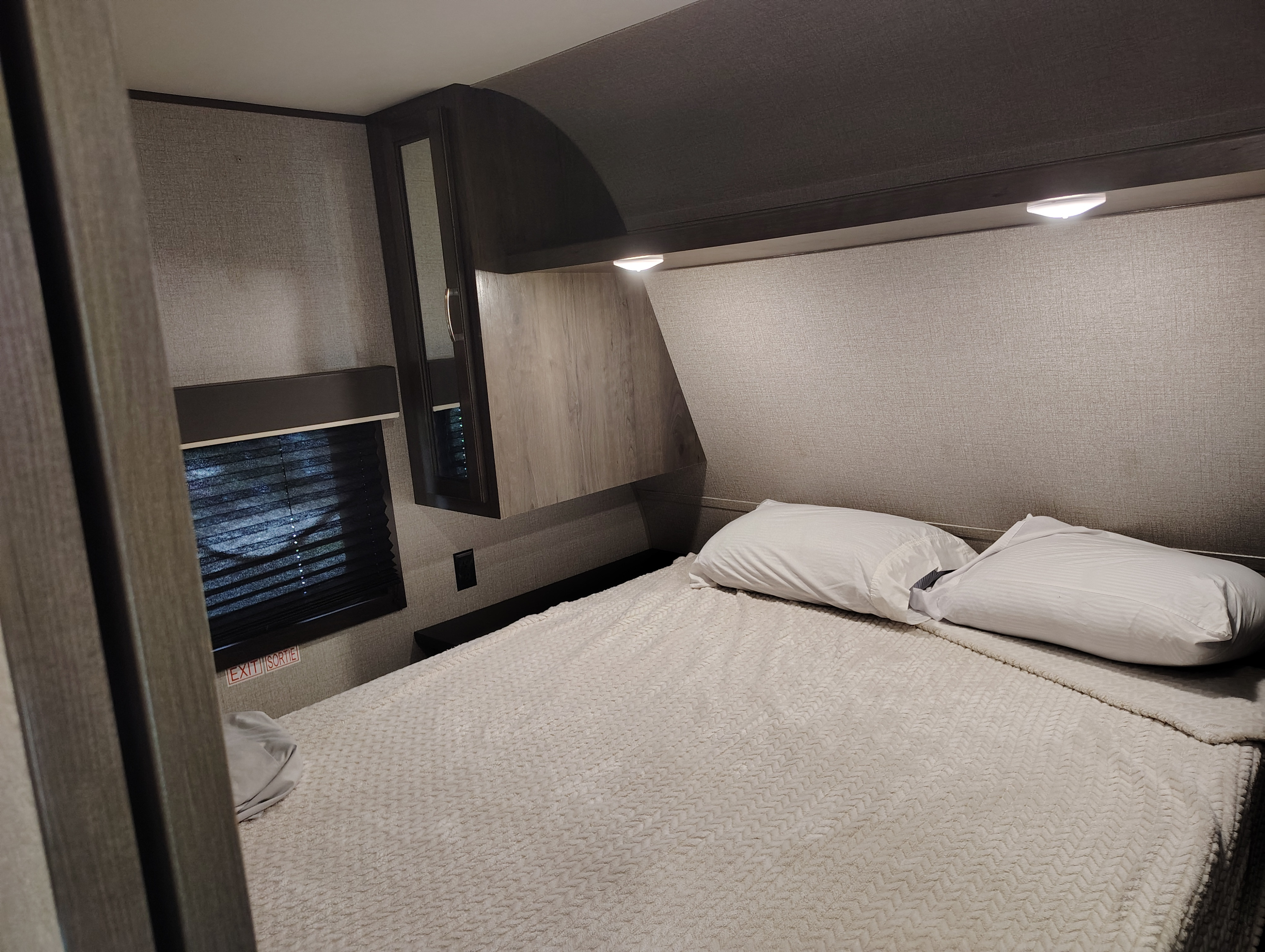 Cozy RV rental bedroom features a textured white bed, two pillows, a side window with blinds, and dark cabinetry.. Jayco Jay Flight SLX 2020
