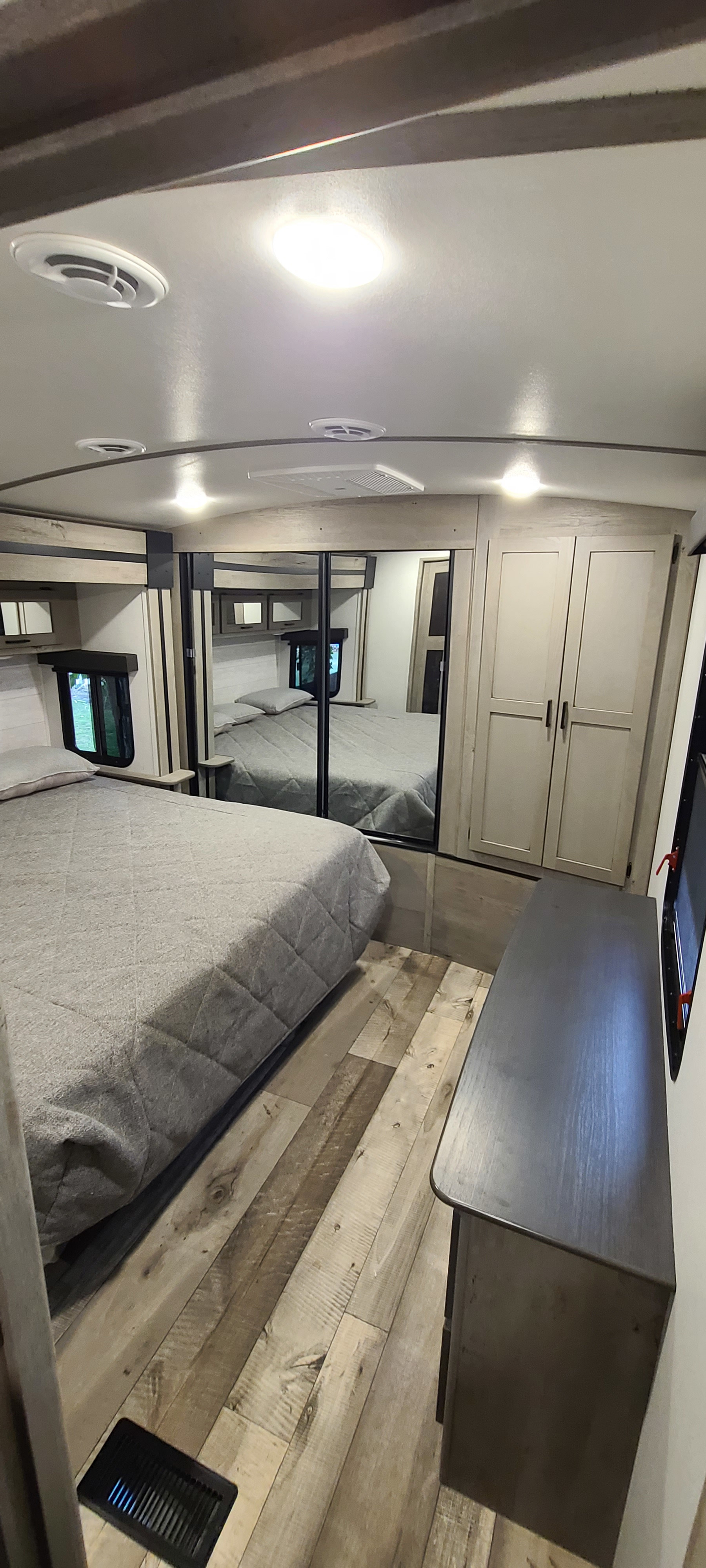 This RV rental bedroom offers a comfortable bed, mirrored closet, sleek dresser, and modern wood-look flooring, creating a cozy travel space.. Keystone RV Outback 2021