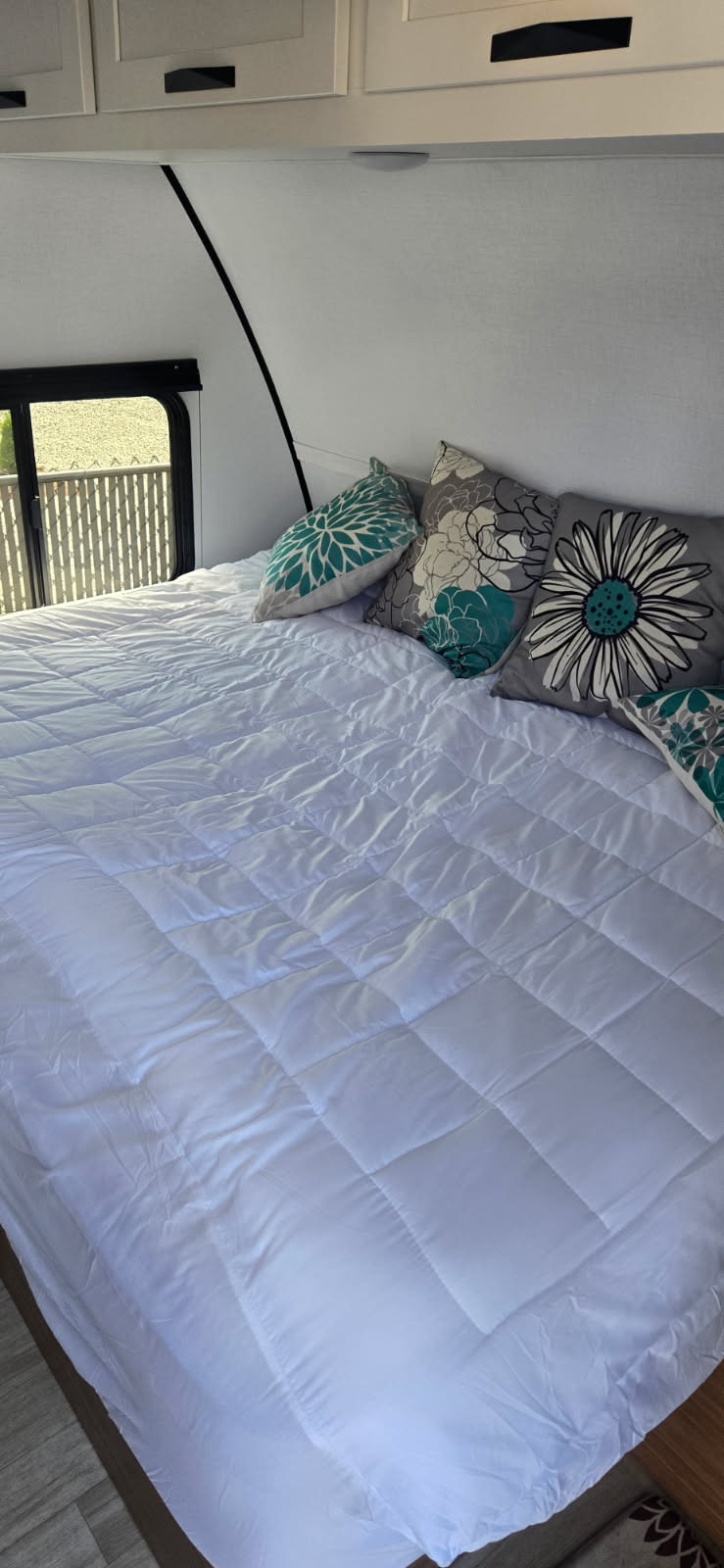 Cozy RV rental bedroom featuring a bed with white quilted bedding and floral accent pillows, perfect for a comfortable stay.. Keystone Passport 190RDWE 2026