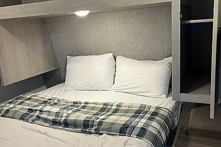 Compact RV rental bedroom with a cozy bed, white pillows, plaid blanket, and convenient built-in storage.. Keystone RV Springdale 2024
