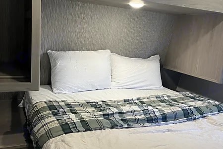 Cozy bed with white pillows and plaid blanket in this RV rental, offering a comfortable sleeping area.. Keystone RV Springdale 2024