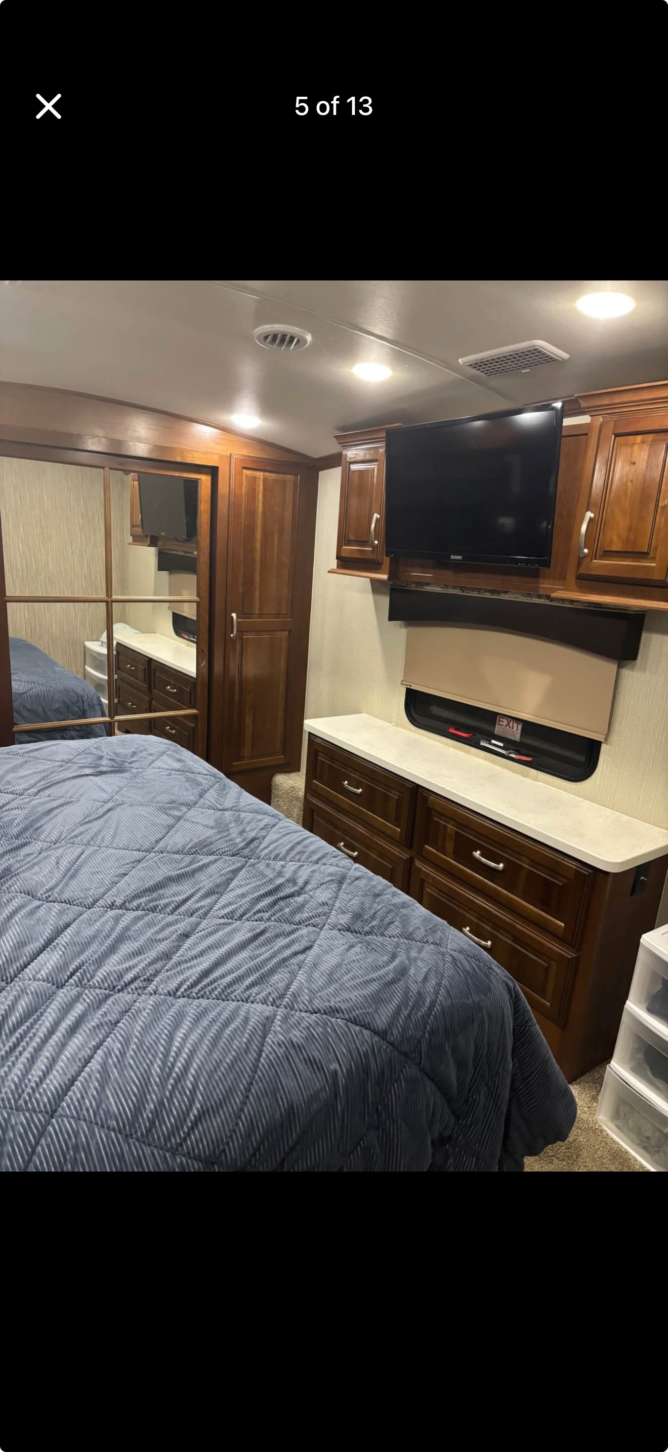 RV rental bedroom interior features a blue bed, mirrored wardrobe, wood cabinetry, wall-mounted TV, and window.. Forest River Cardinal 2018