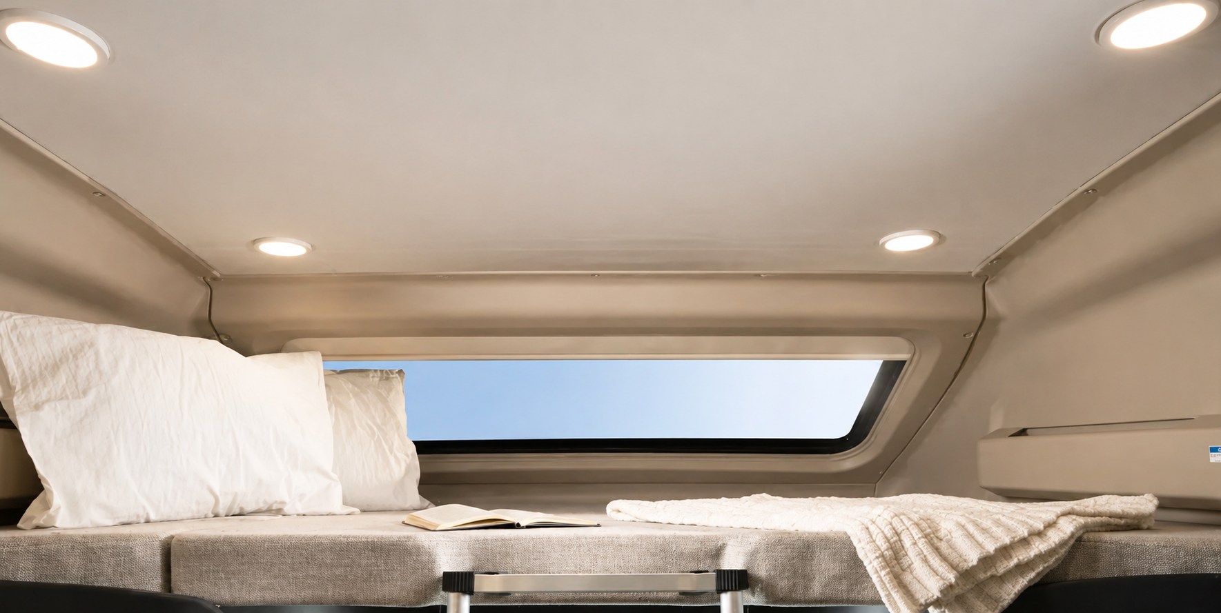 Over-cab sleeping area in an RV rental, featuring a comfortable bed with pillows, blanket, book, and sky views from the window.. Entegra Coach Qwest 2021