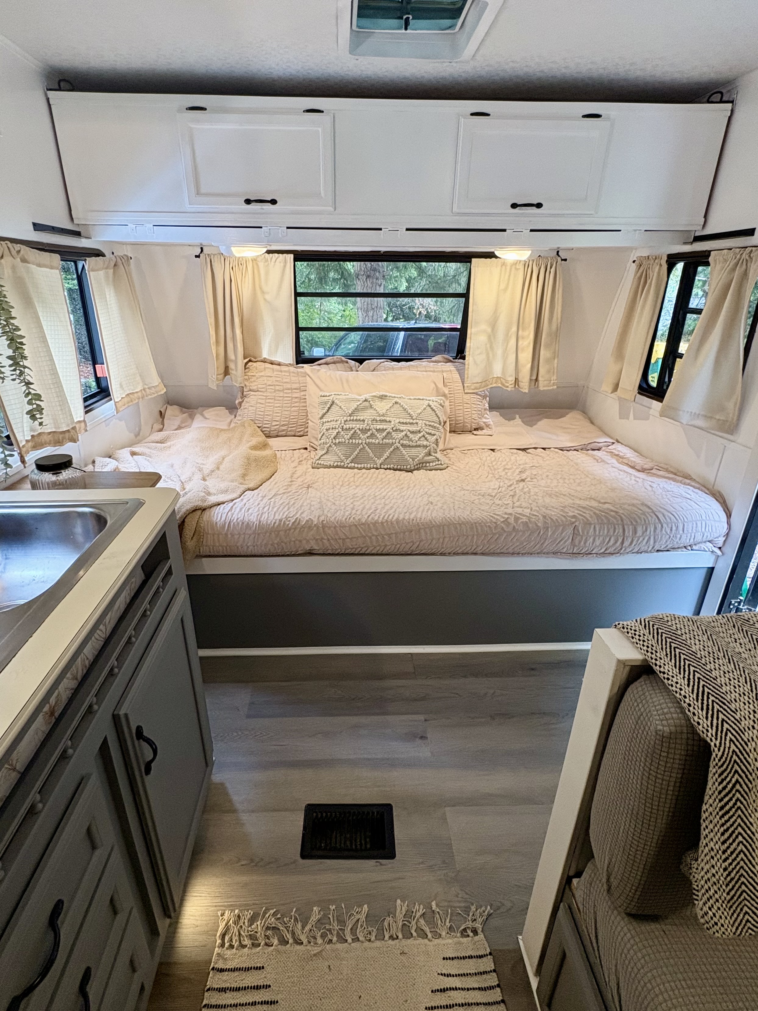 Inside a renovated RV rental: a bright, cozy bedroom with blush bedding, overhead white cabinets, and a compact sink area.. Dutchmen Classic 1993