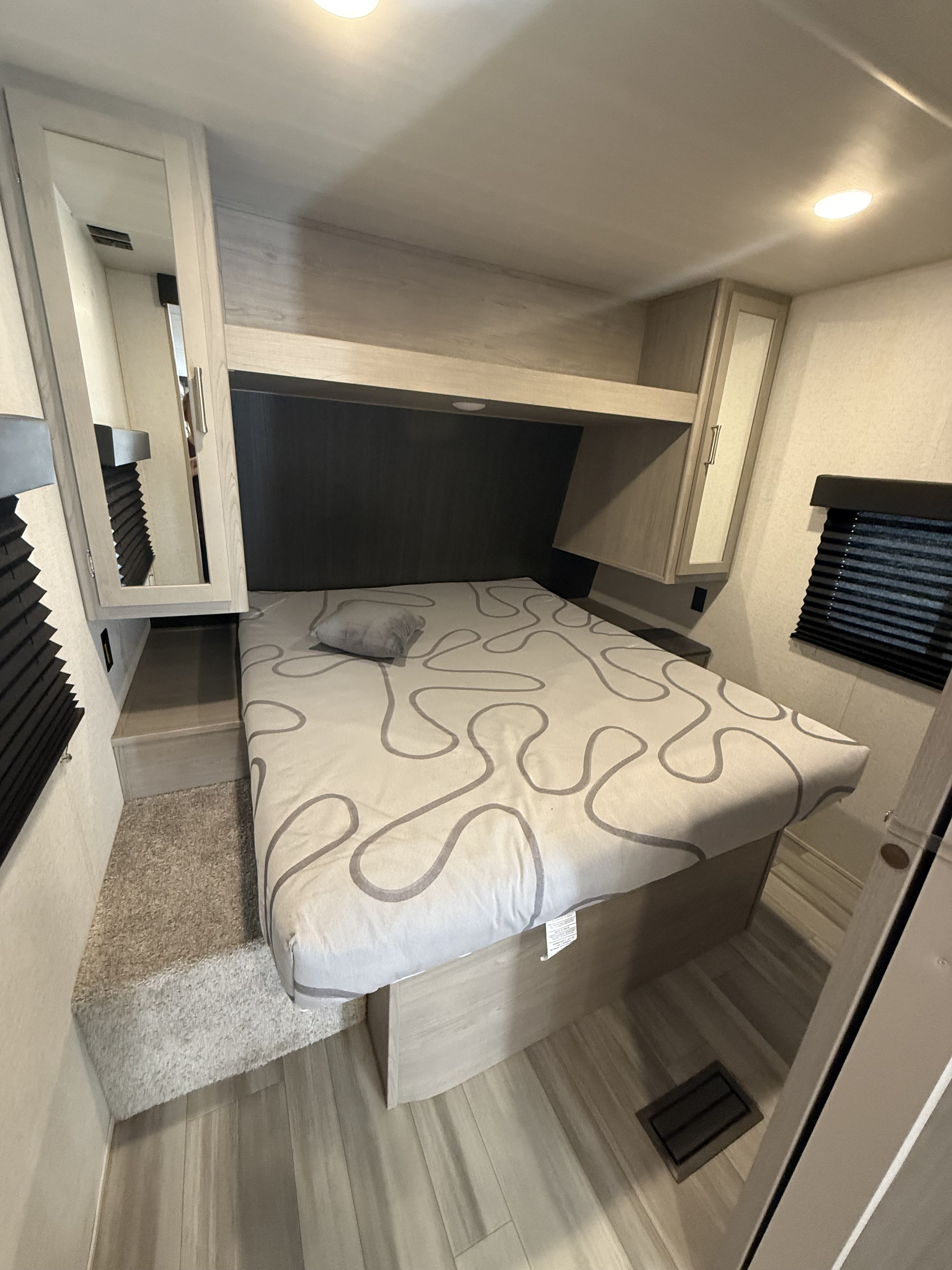 Cozy RV rental bedroom with patterned bed, overhead storage, mirrored cabinets, and blinds, offering comfortable travel.. Springdale SG240RB 2024