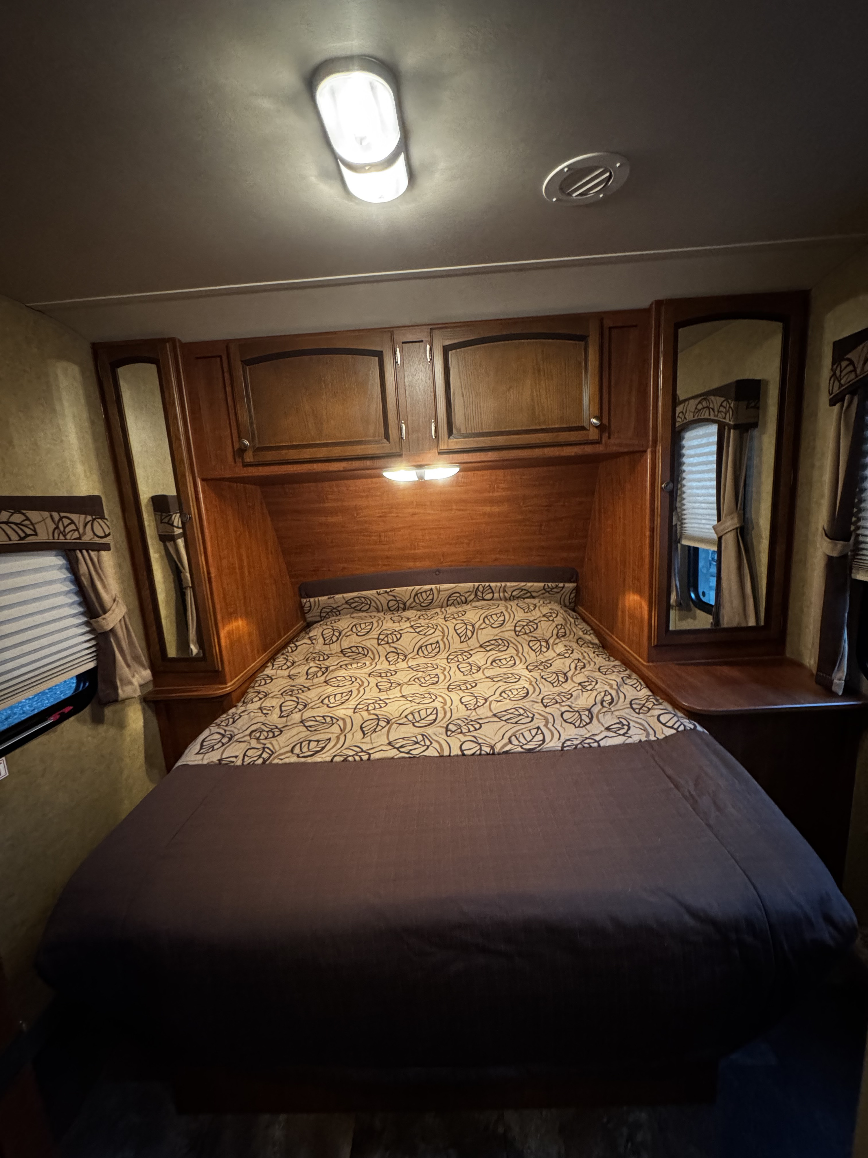 Compact RV rental bedroom interior with a patterned bed, overhead wooden cabinets, bedside mirrors, and dim lighting.. Jayco White Hawk Ultra Lite 2013