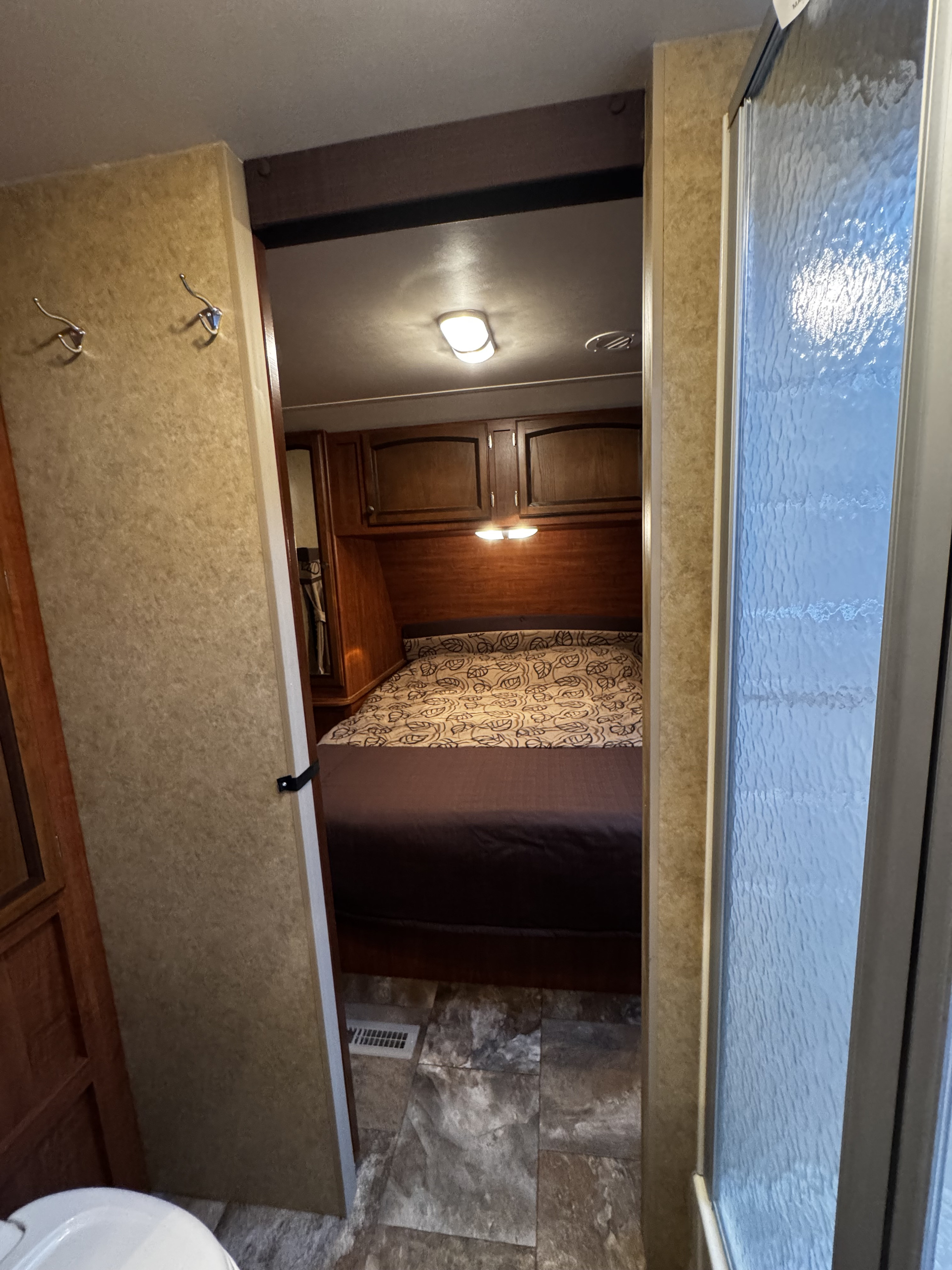 RV rental: Looking from the bathroom past hooks & a textured shower into a bedroom with a patterned bed, cabinets, and lights.. Jayco White Hawk Ultra Lite 2013