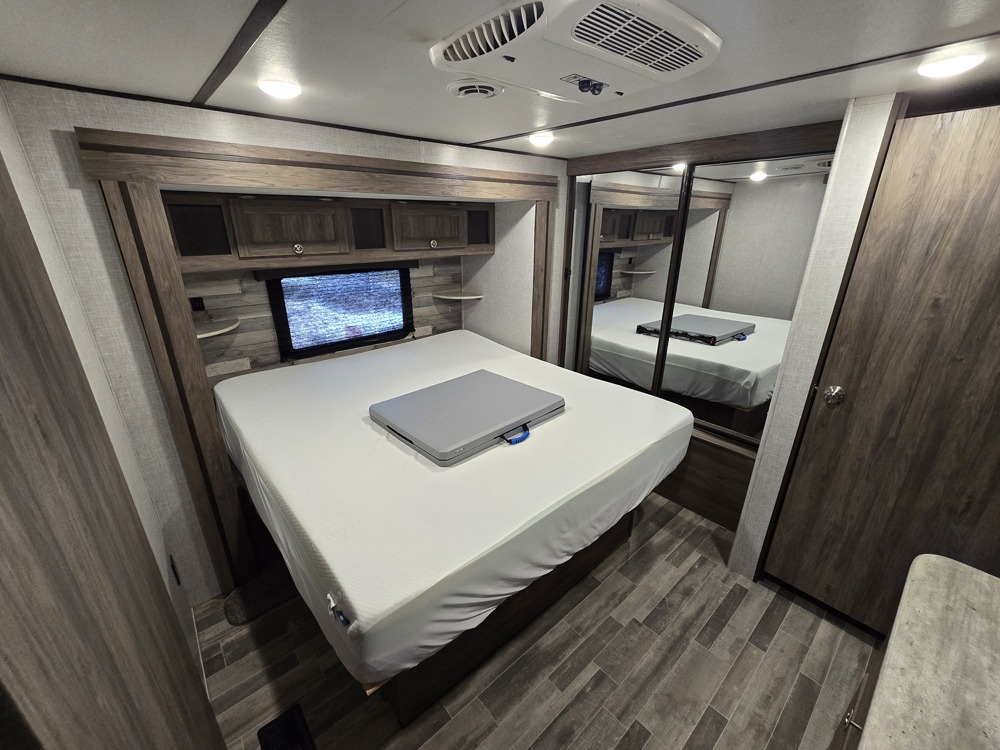 RV rental bedroom featuring a comfortable bed with overhead storage, a window, and mirrored wardrobe. Spacious interior.. Crossroads RV Longhorn 2021
