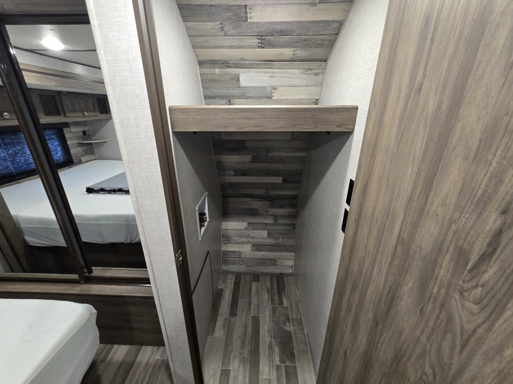 An RV rental's compact interior showing a storage space with utility hookups and a mirrored bedroom view.. Crossroads RV Longhorn 2021