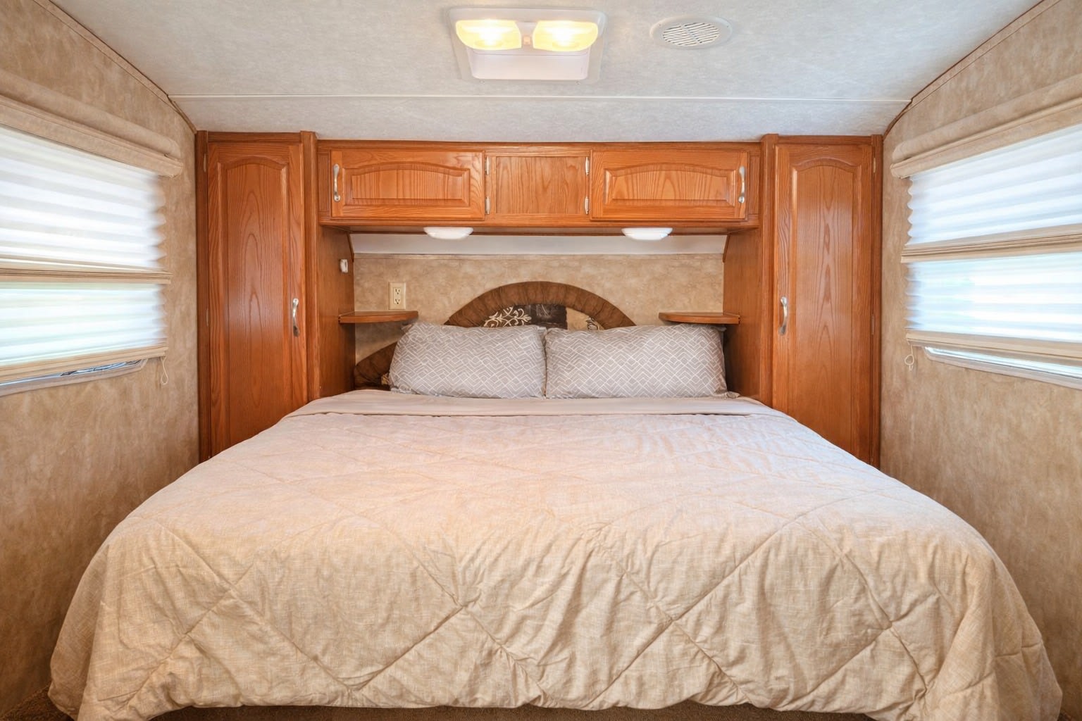 Comfortable RV rental bedroom with a queen bed, overhead cabinetry, and side windows with blinds, offering cozy travel accommodations.. Keystone RV Copper Canyon 2007