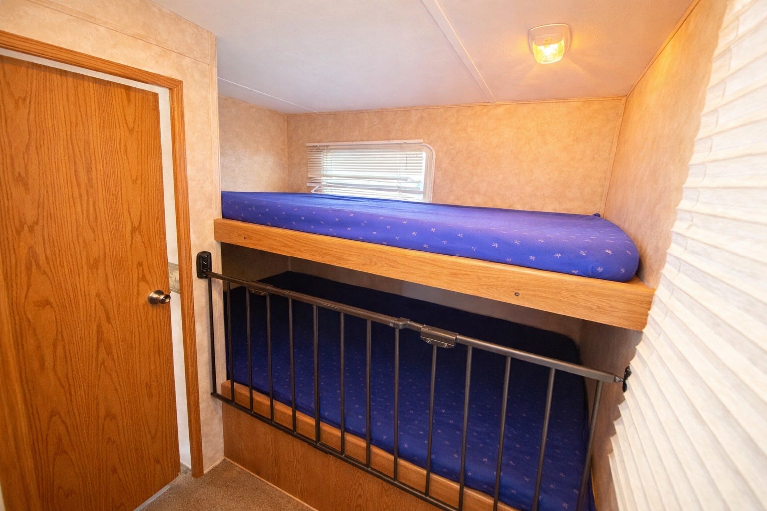 RV rental bunk beds: two blue mattresses, metal safety rail on lower bunk. Wooden door and window with blinds visible.. Keystone RV Copper Canyon 2007
