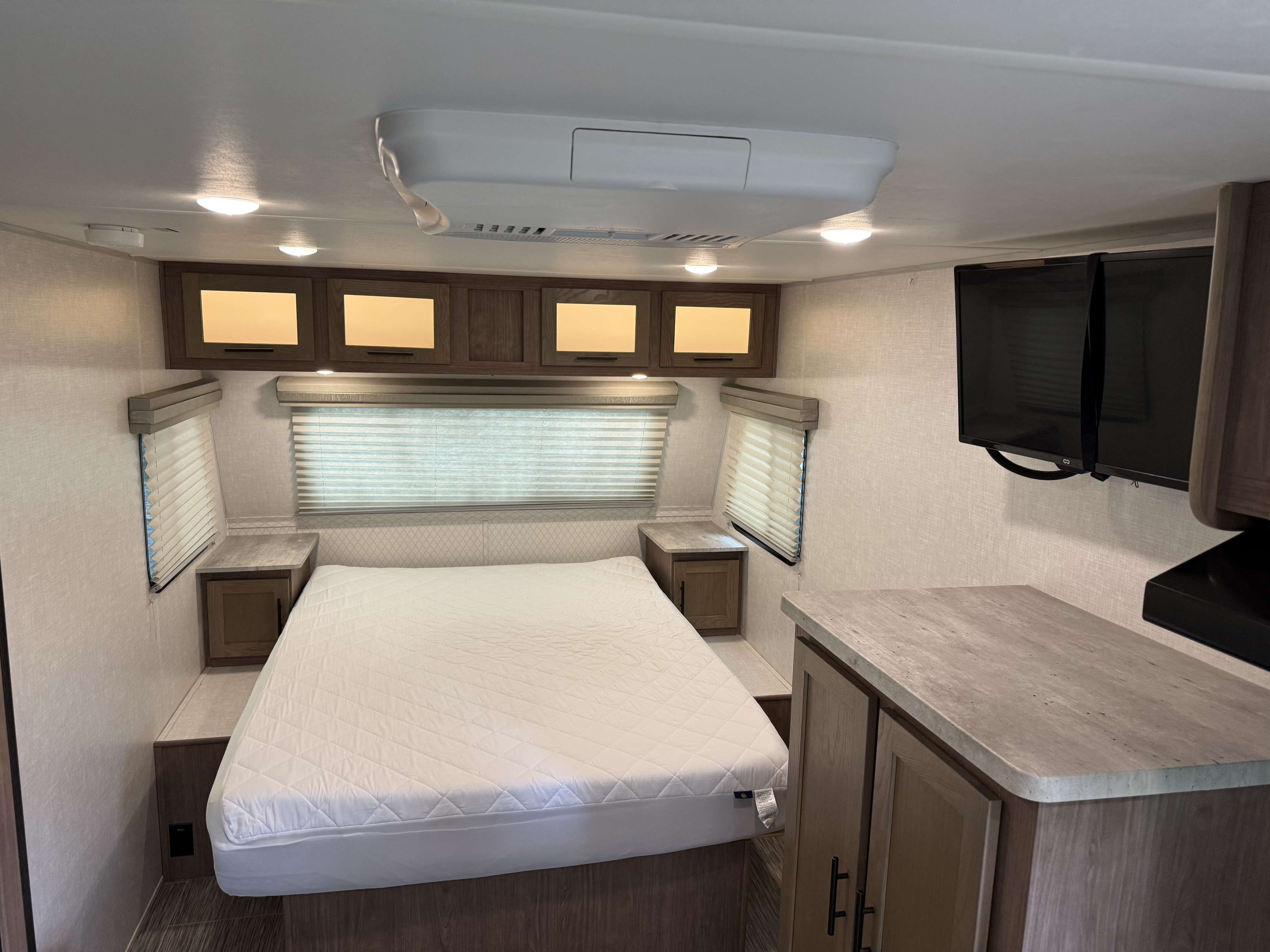Modern rv rental bedroom featuring a queen bed, bright overhead lights, storage cabinets, and a mounted TV.. Forest River R-Pod 2020