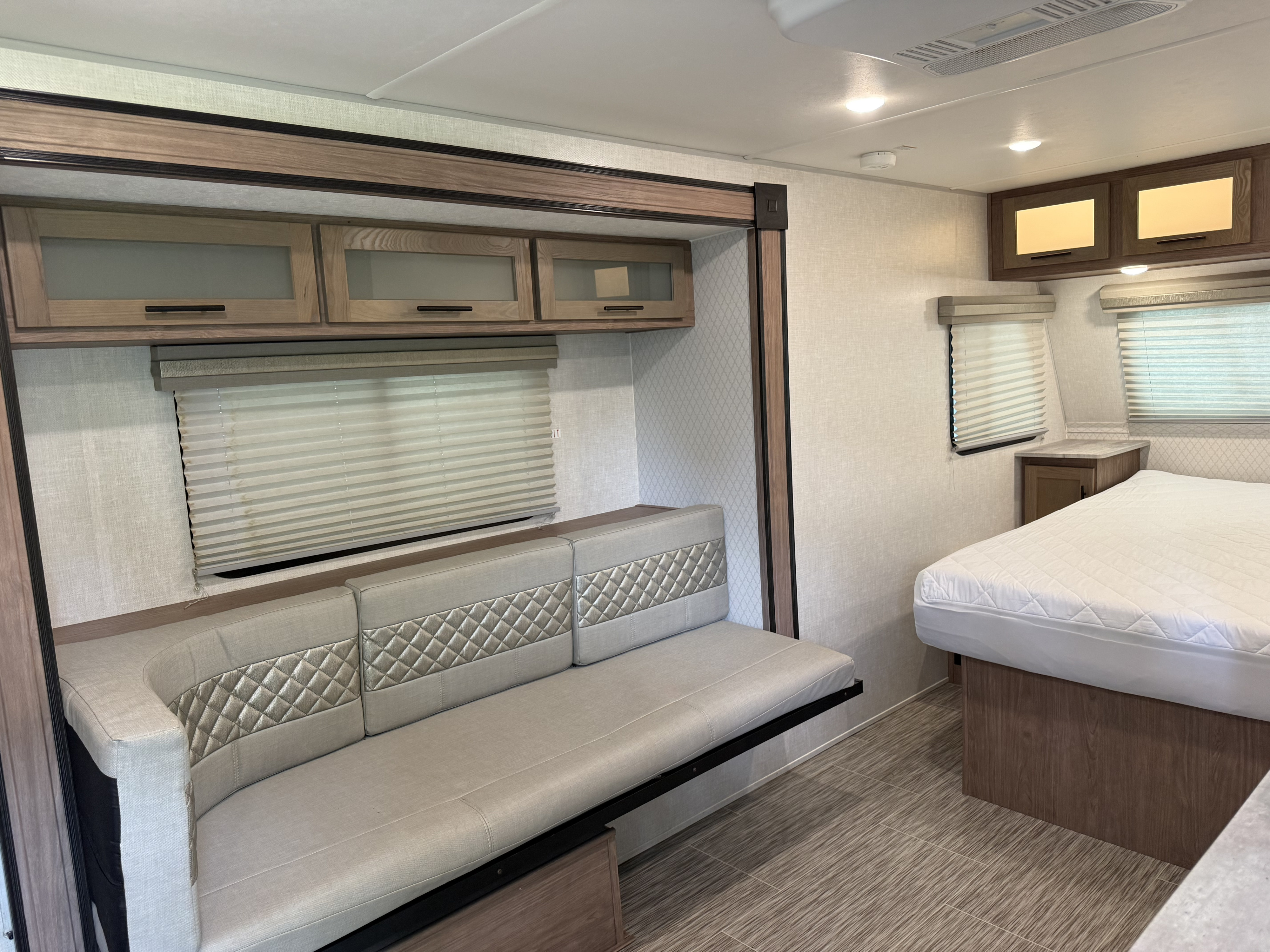 RV rental interior featuring a modern sofa with quilted accents, overhead cabinets, and a comfortable bed for travel.. Forest River R-Pod 2020