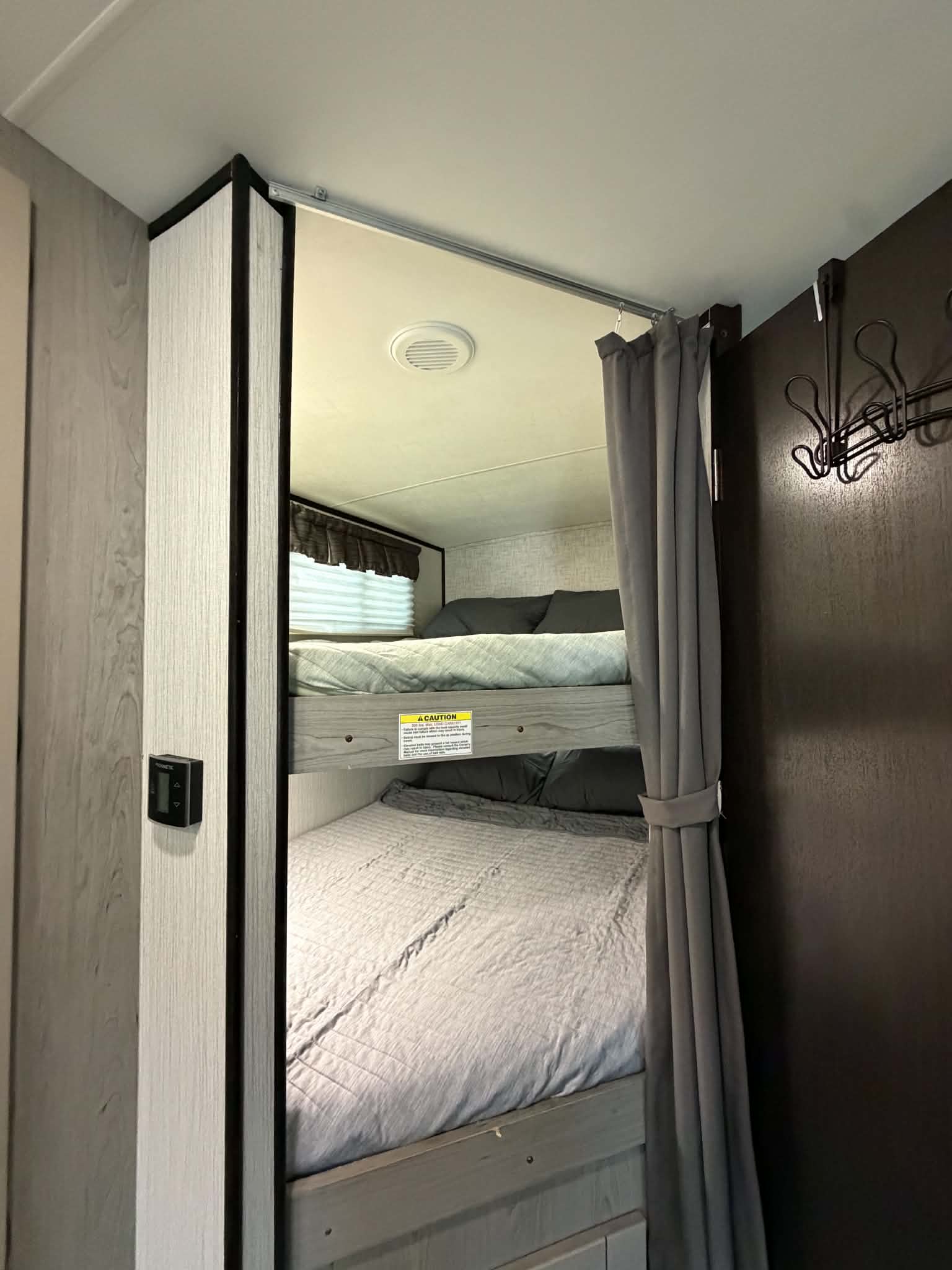 RV rental interior showing comfortable bunk beds with soft bedding, a privacy curtain, and a climate control panel.. Heartland RVs Mallard 2020