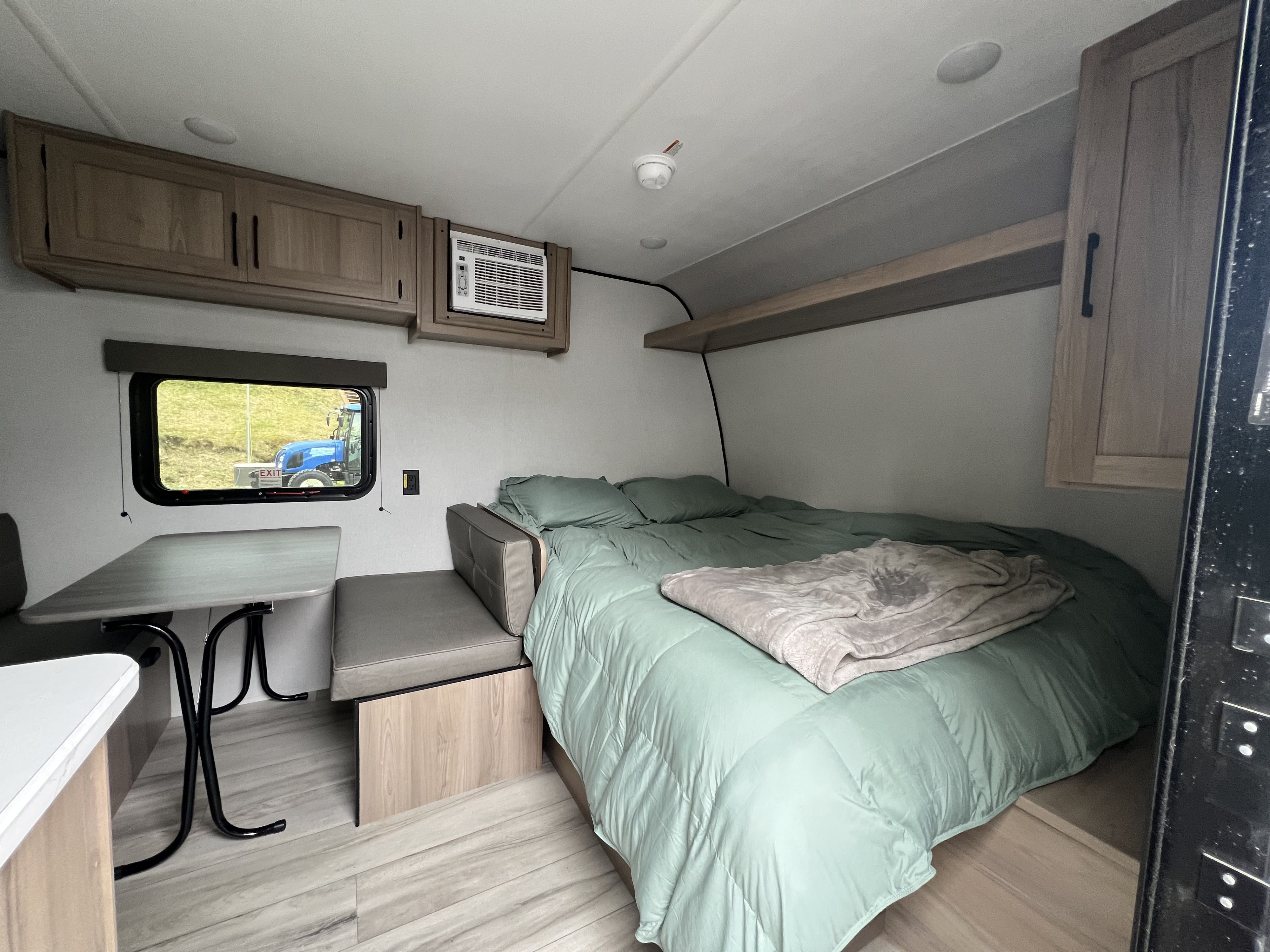 Cozy rv rental interior with bed, dining, AC, and storage. A blue tractor is visible outside the window.. Keystone RV Coleman 17B 2026