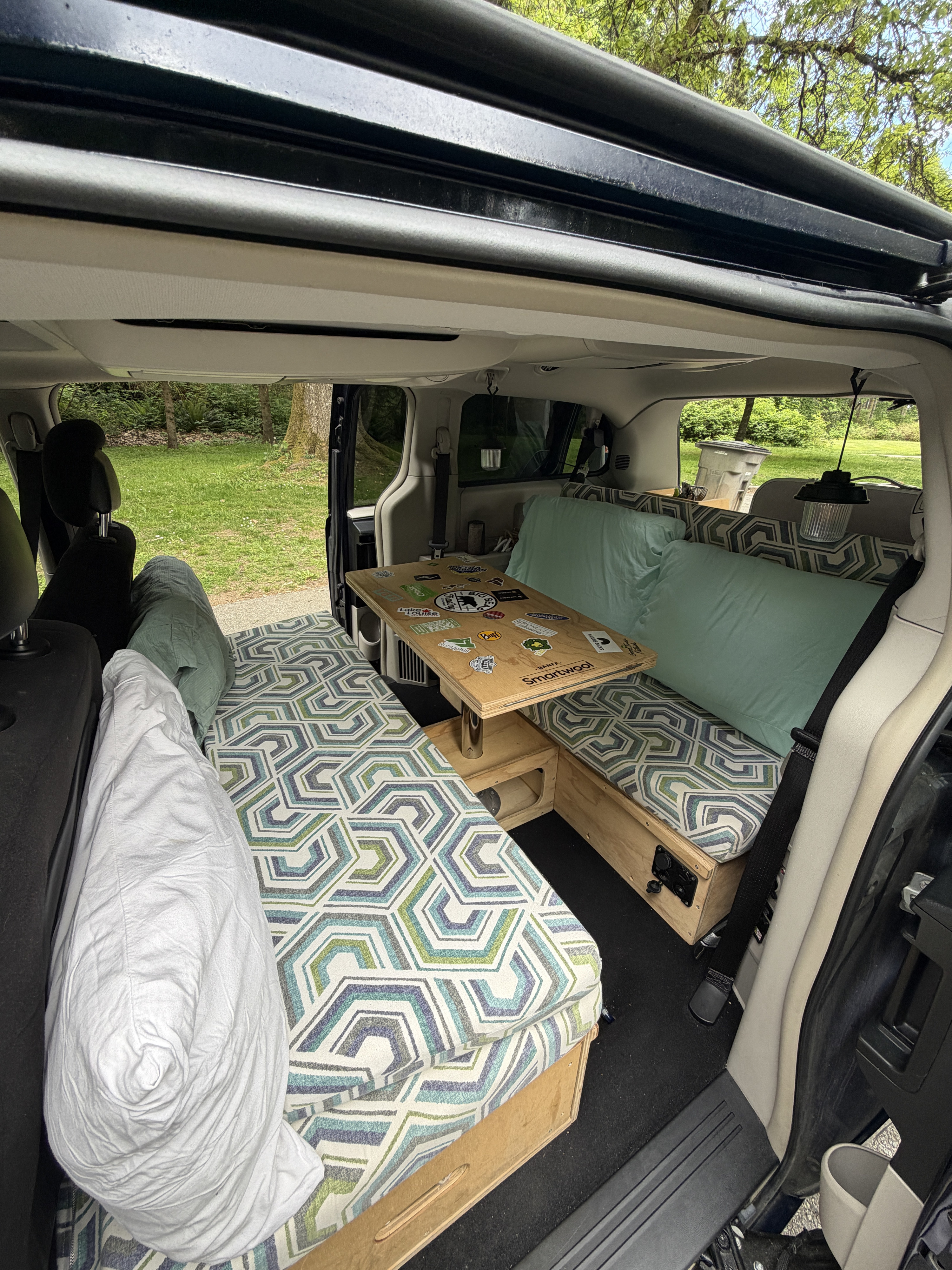 View inside an rv rental camper van setup with patterned cushions, pillows, and a sticker-laden table, creating a cozy living space.. Chrysler Town & Country 2014
