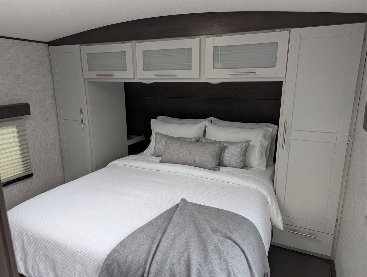 Modern RV rental bedroom: comfortable bed with white linens, overhead & side storage cabinets. Clean & compact space.. Keystone RV BULLET 2021