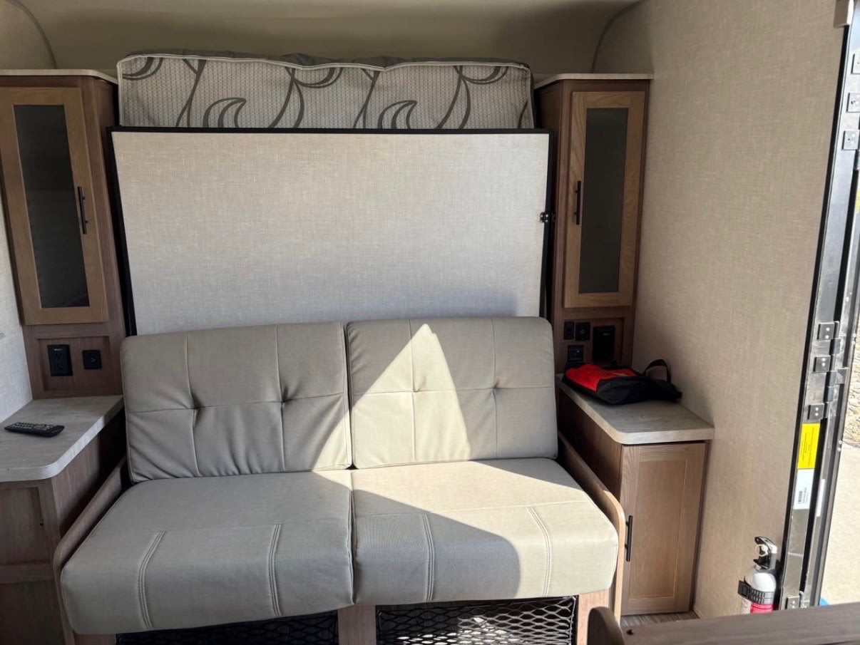 RV rental interior featuring a convertible sofa below a stored Murphy bed, flanked by wood cabinetry.. No Boundaries 19 2020