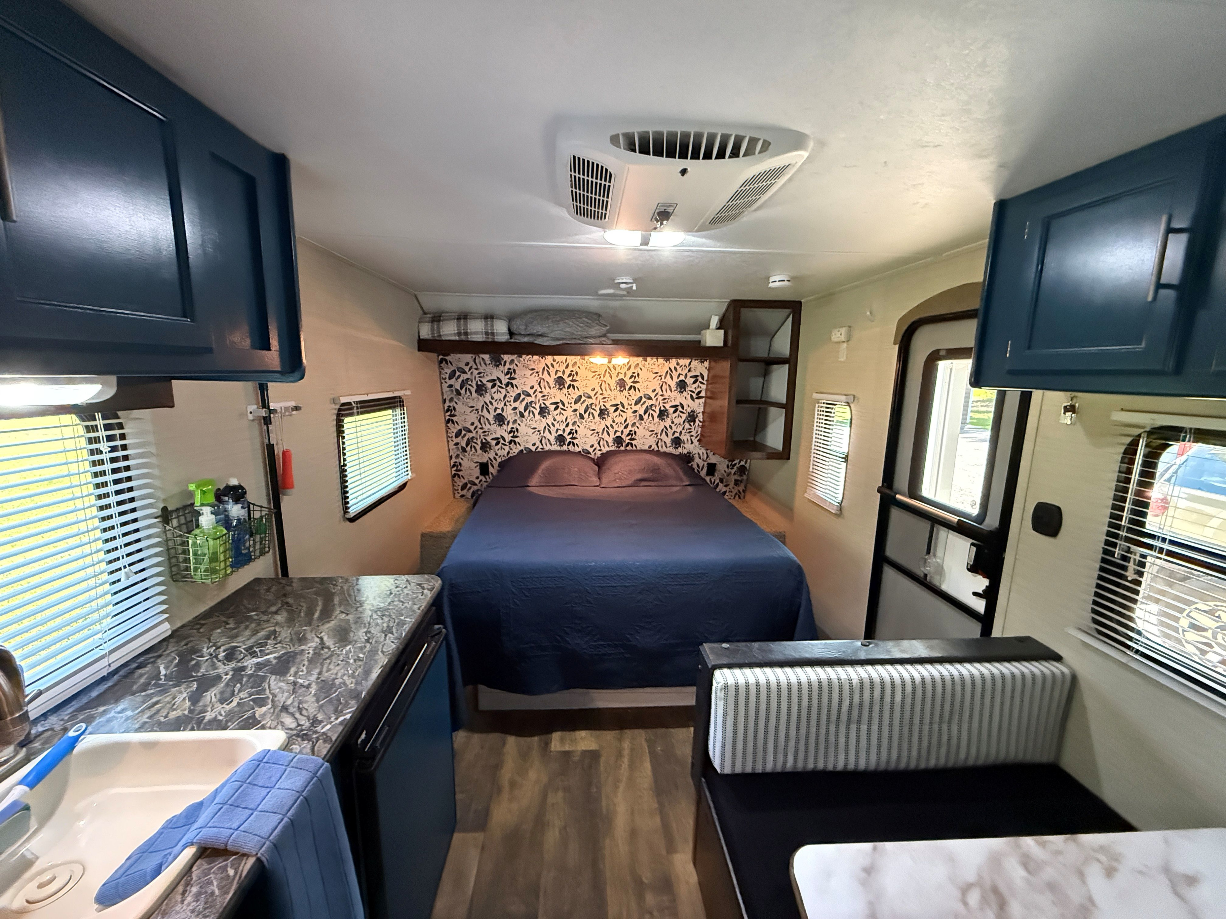 RV rental interior: A cozy blue bed with floral backdrop, compact kitchen with sink, and striped dinette. Ready for adventure.. Keystone RV Summerland Mini 2016