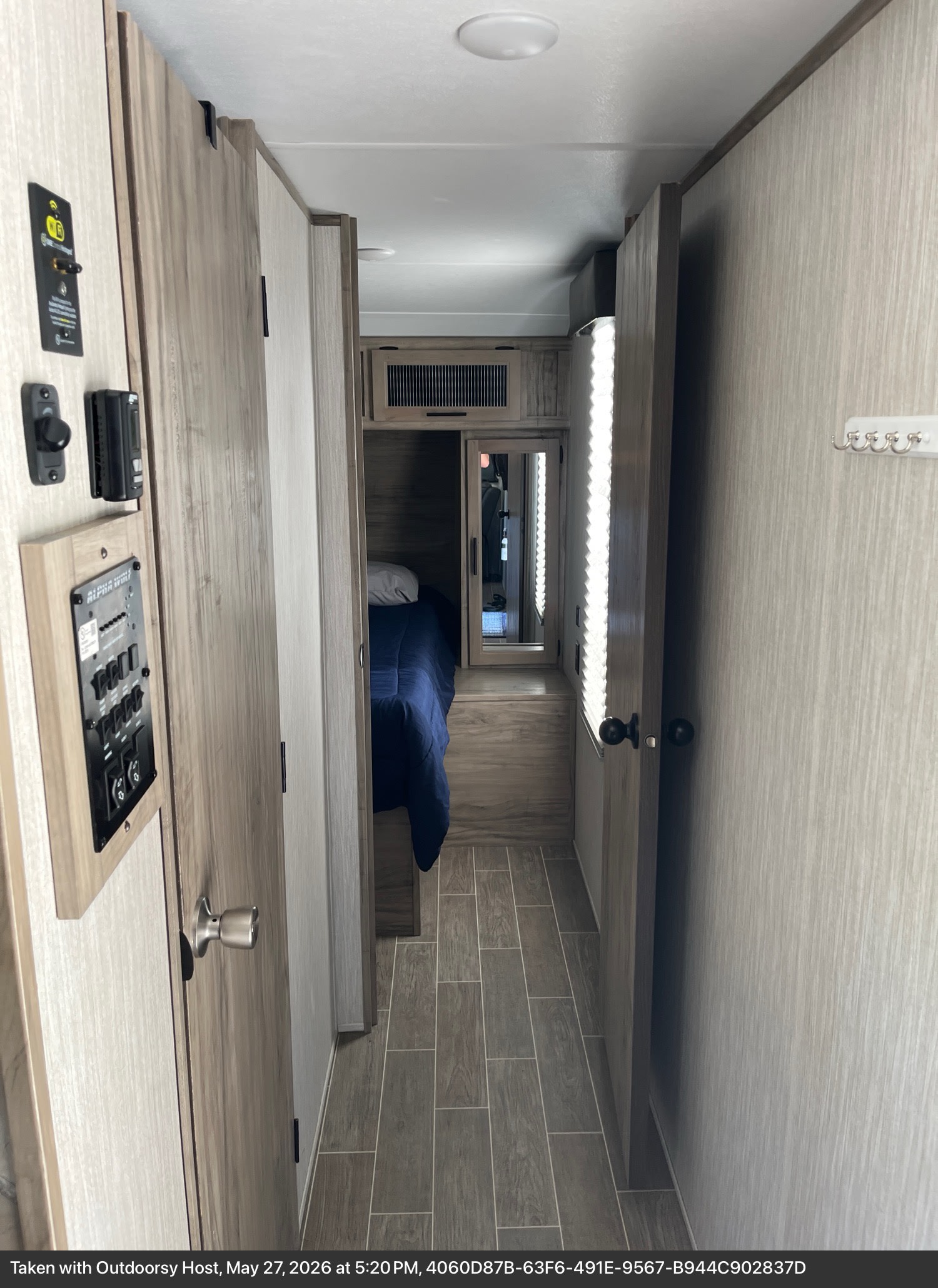 RV rental interior: A compact hallway with control panels leads to a cozy bedroom featuring a blue comforter and mirror.. Forest River Cherokee Alpha Wolf 2021
