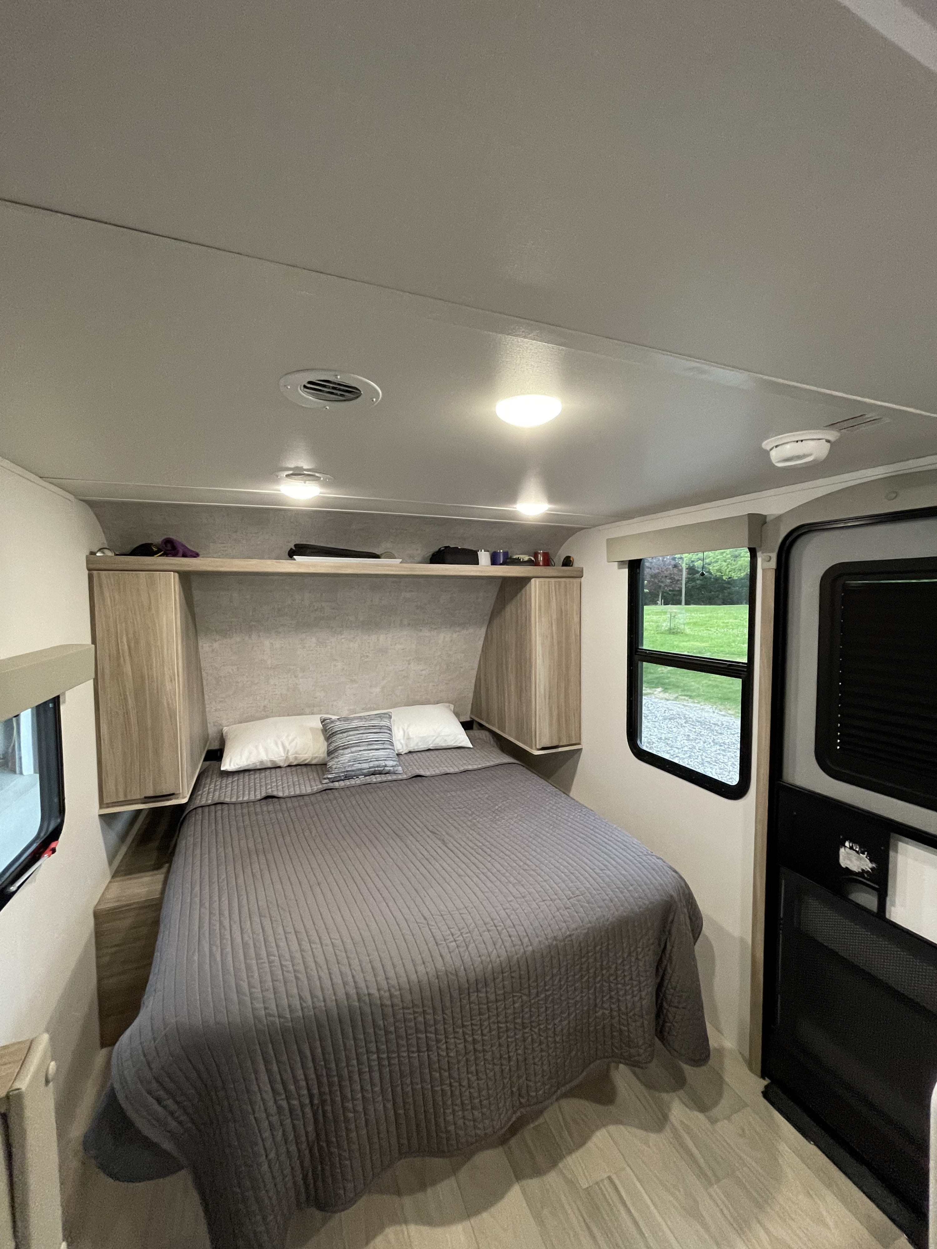 This cozy RV rental bedroom features a comfy bed with gray bedding, overhead storage, and windows offering natural light.. Winnebago M Series 2025